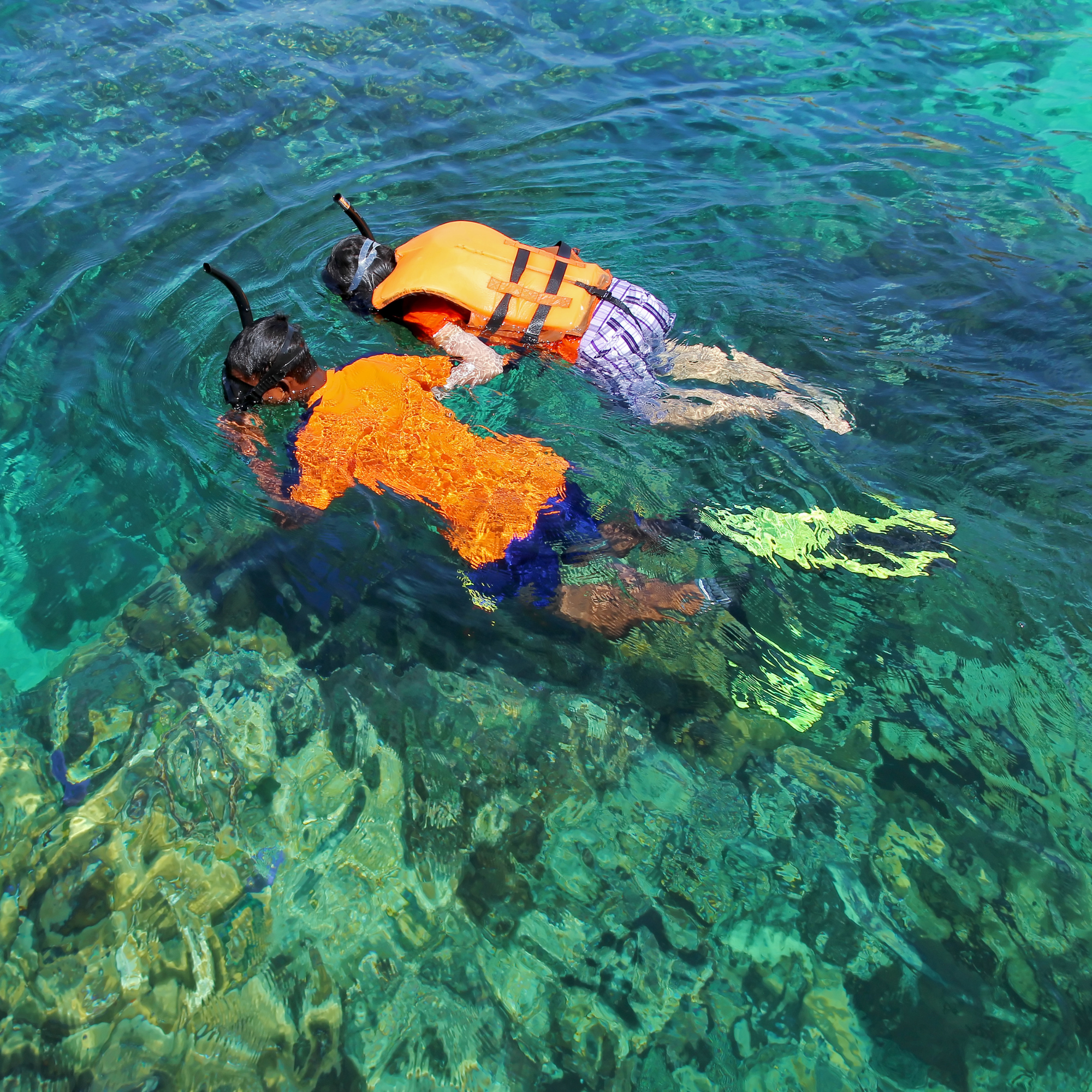 Dos niños con snorkel y chaleco salvavidas explorando en aguas claras del océano