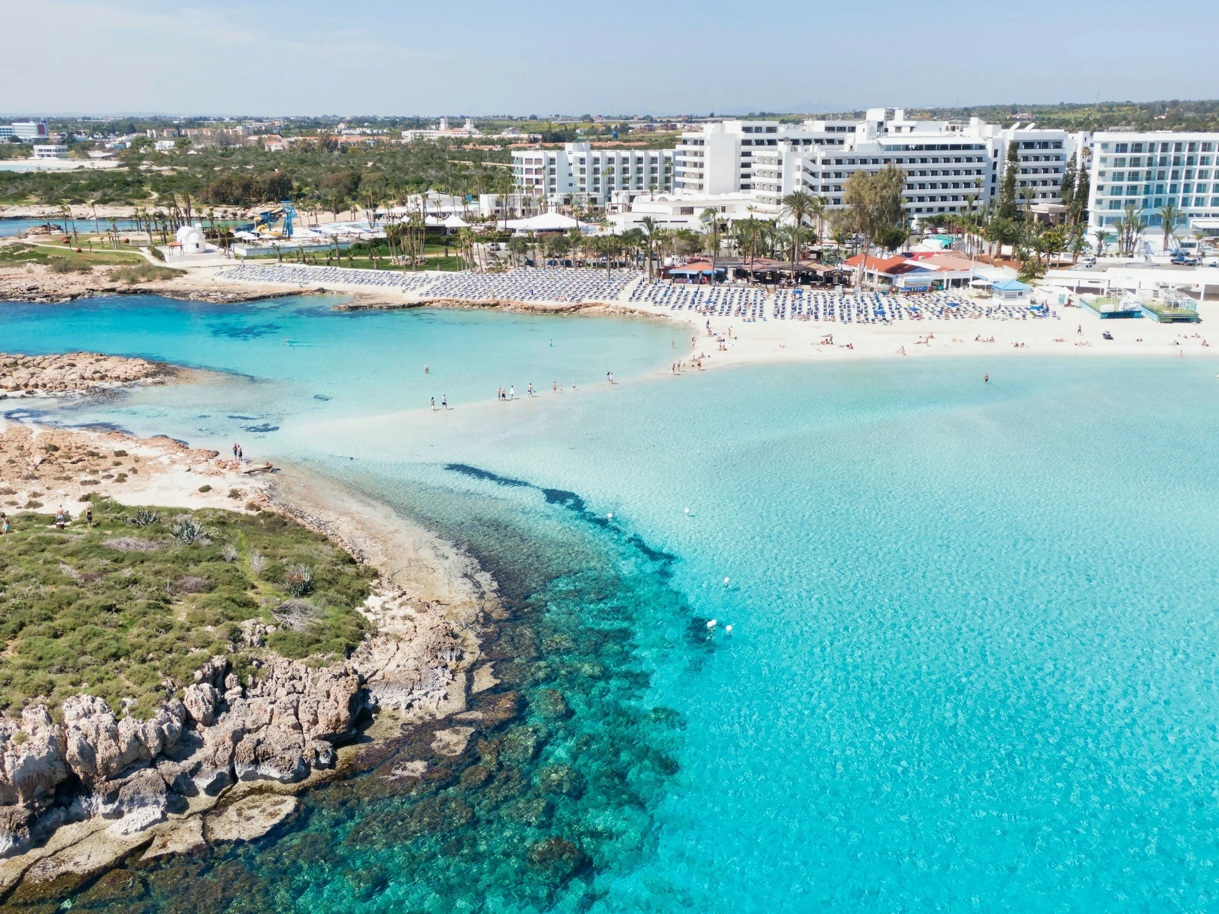 Aerial view of an all-inclusive beach resort with turquoise water, a sandy shoreline, and white resort buildings.