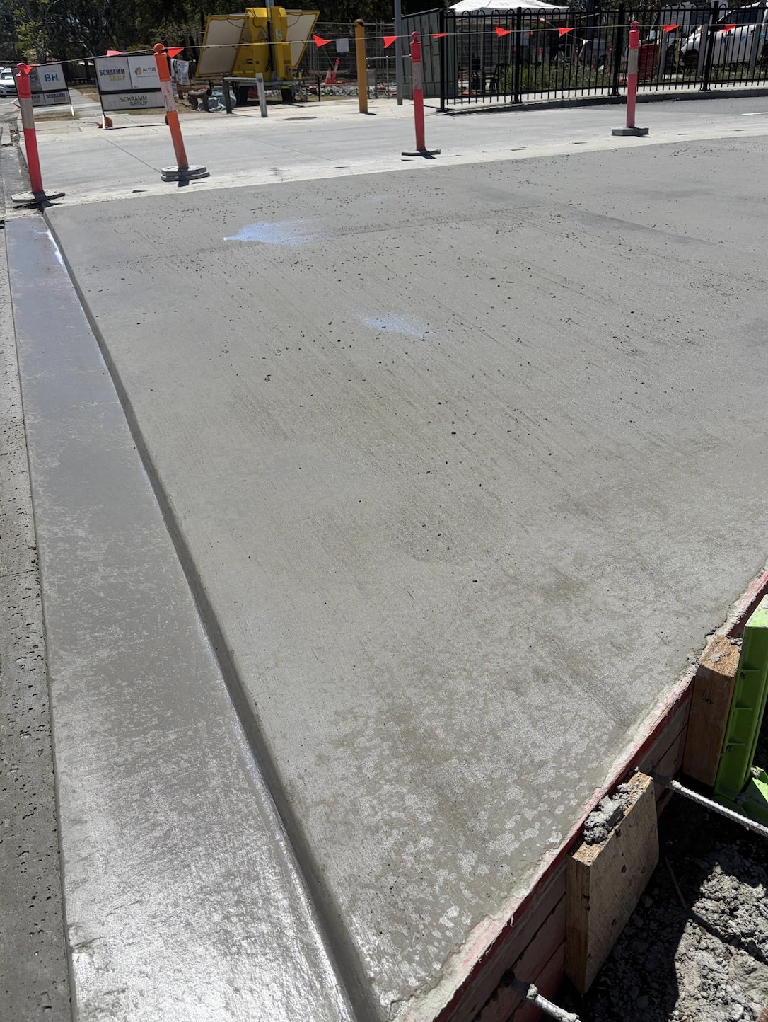 Freshly poured concrete on a sidewalk or driveway with construction barriers and equipment in the background.