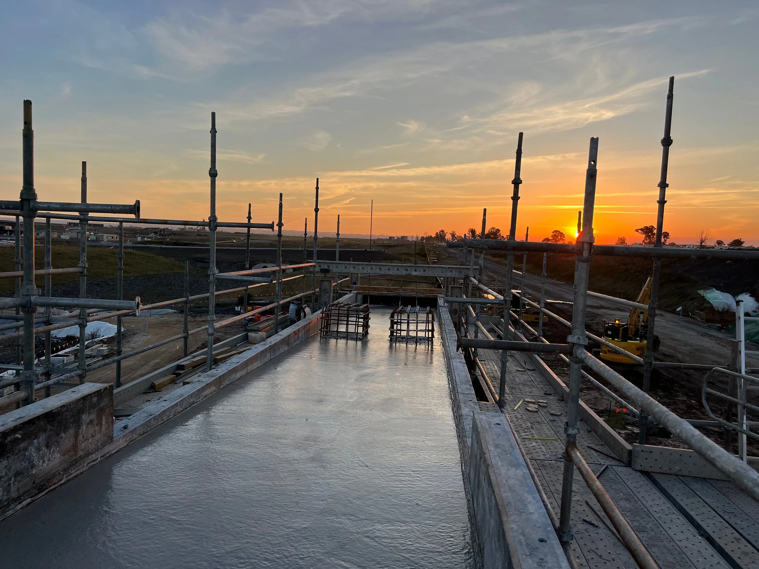 Construction site during sunset with scaffolding and concrete structure, with the sky showing orange and blue hues.