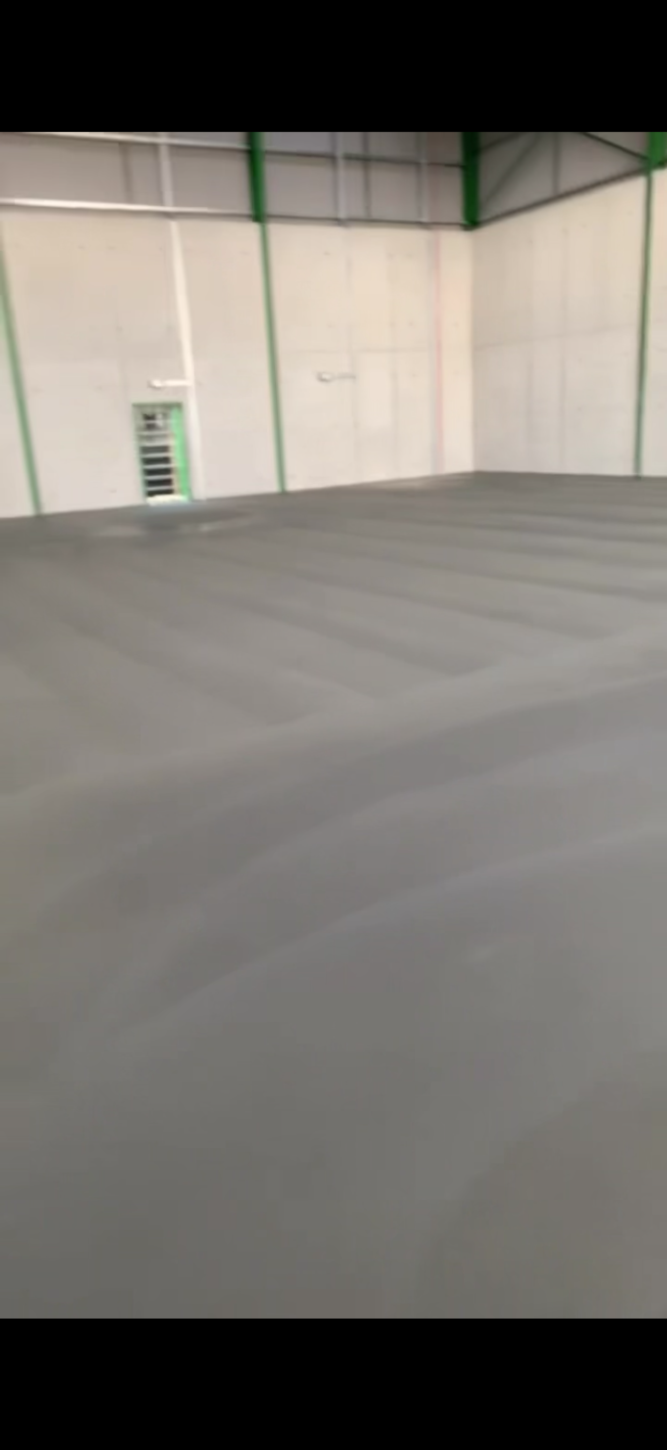 Interior of an empty warehouse or industrial space with white walls, ceiling, and gray floor, with green and white structural supports.