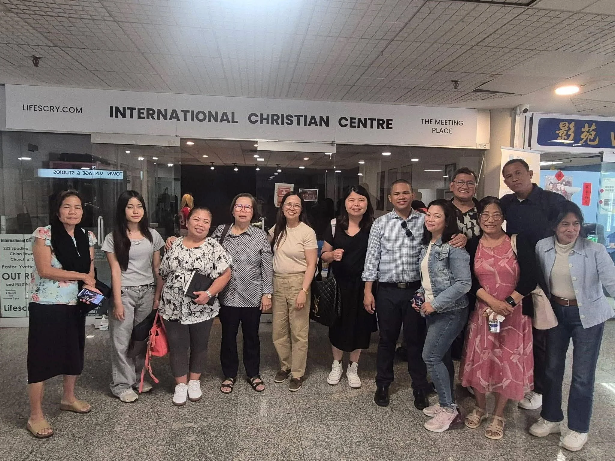 Group of diverse adults posing together in front of the International Christian Centre sign at an airport.