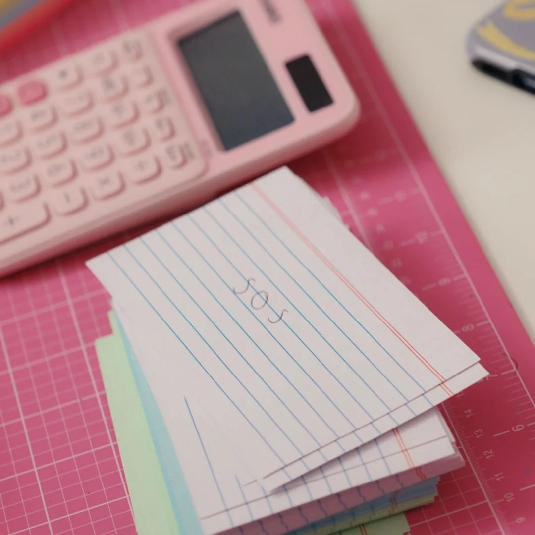A pink calculator and a stack of index cards with the word 'Sad' written on the top card, placed on a pink cutting mat.