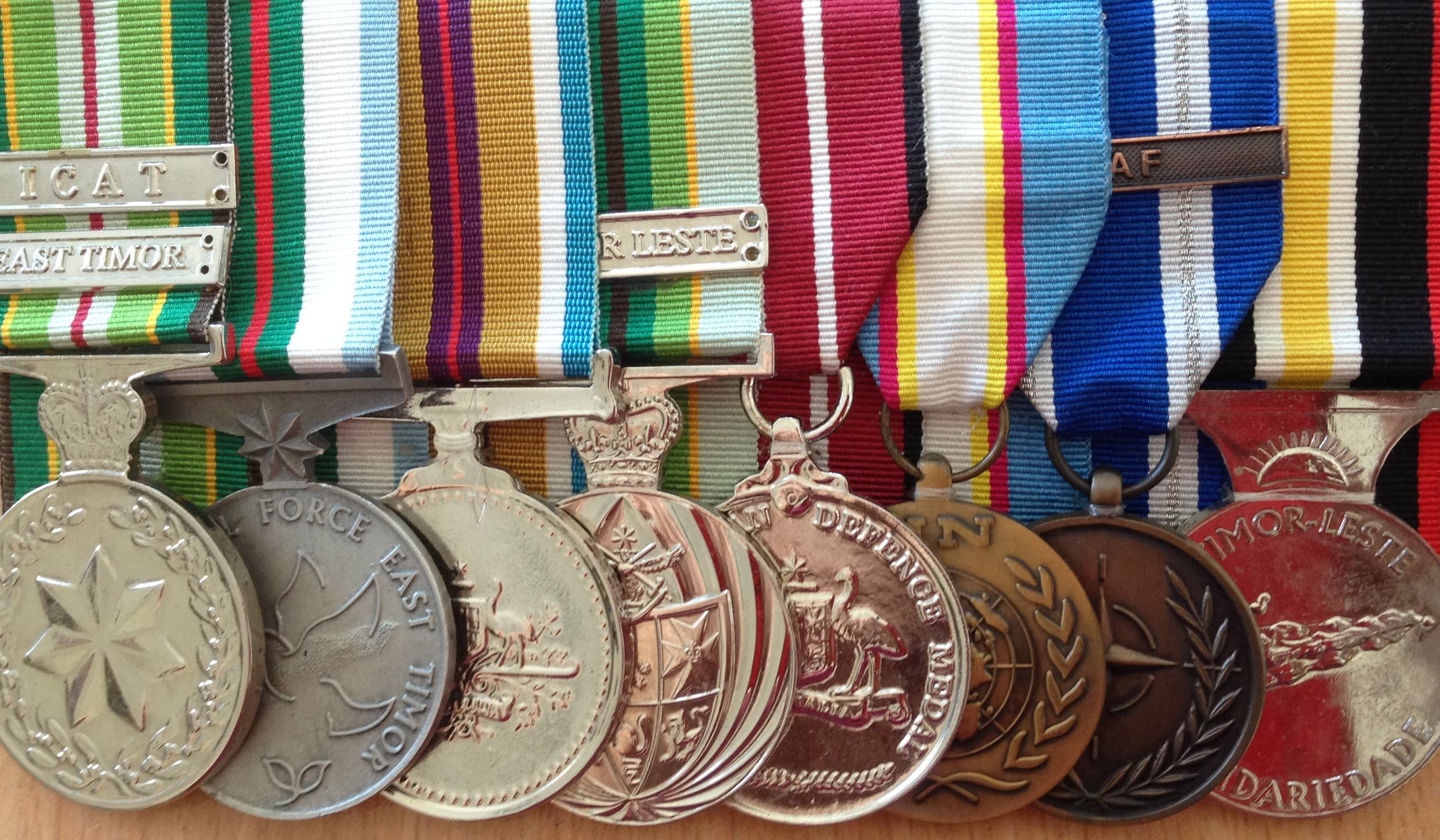 Close-up of military medals and ribbons, showing silver medals with various designs and colorful striped ribbons attached.