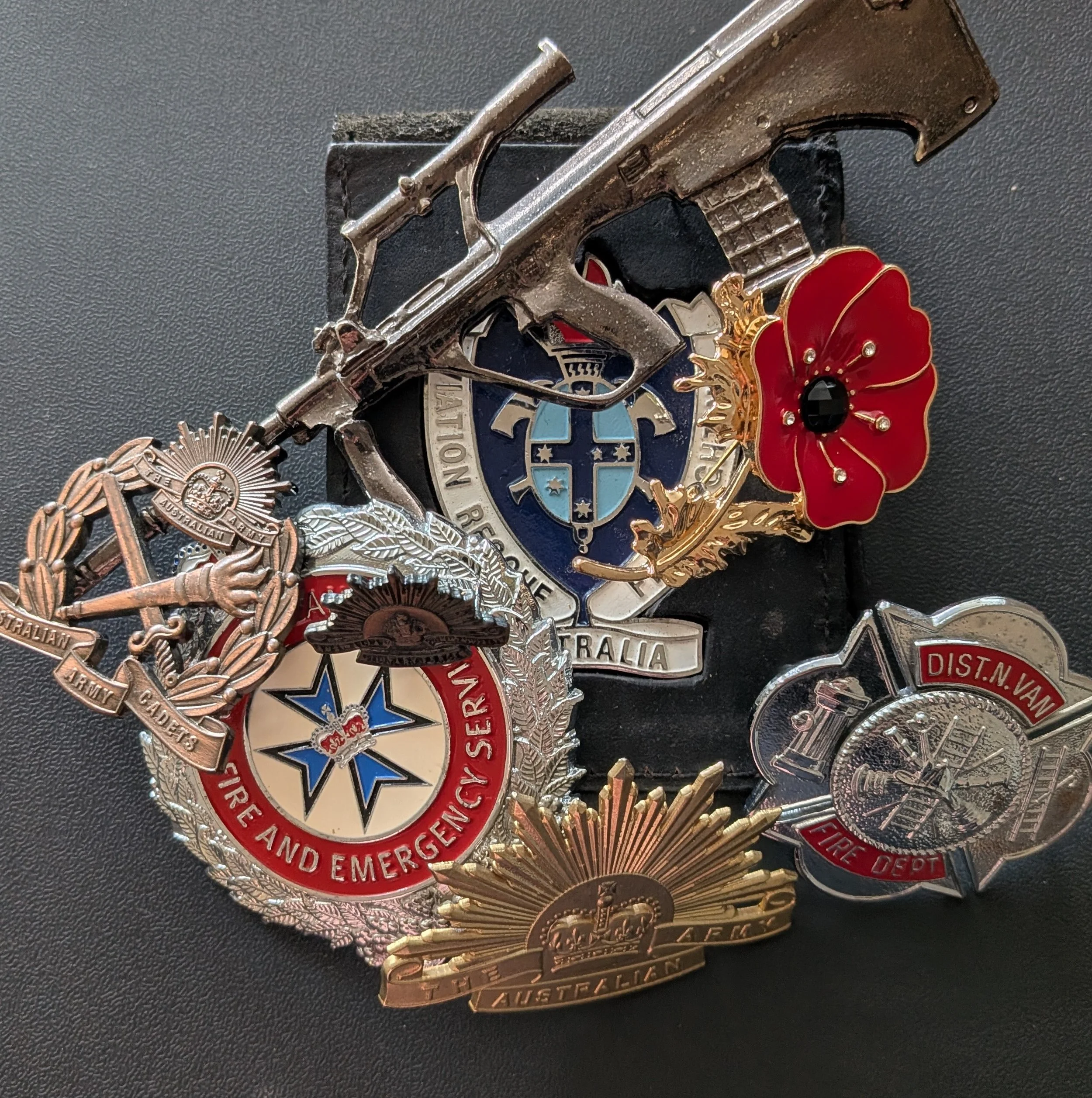Close-up of various military medals and badges, including pins from Australian Army and emergency services, arranged on a black surface.
