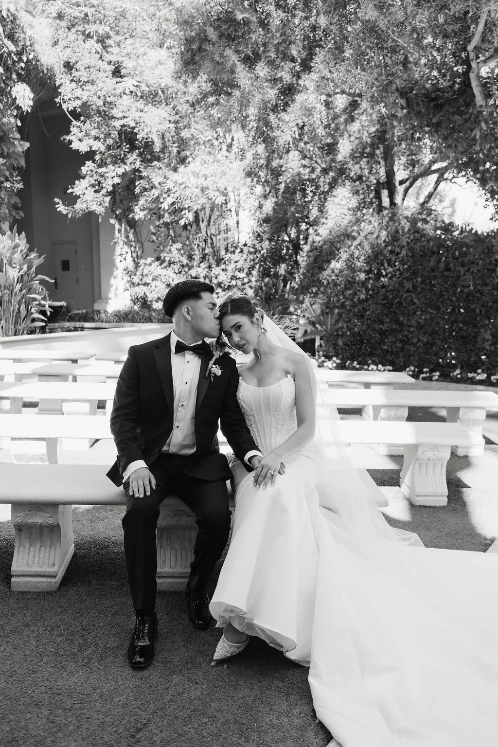 Bride and groom seated together for a timeless black-and-white wedding portrait in a garden courtyard.