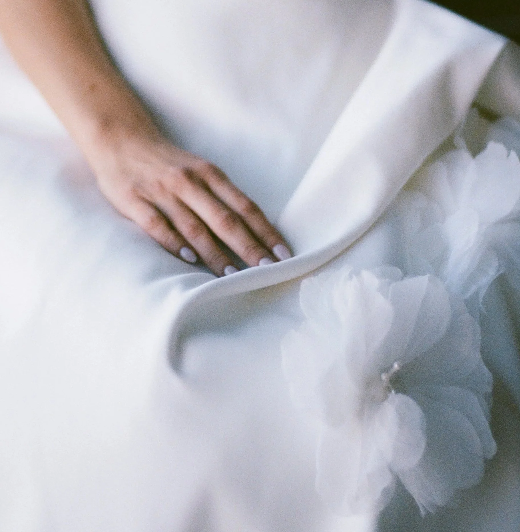 Close-up of a person's hand with manicured nails resting on white fabric with ruffled detail.