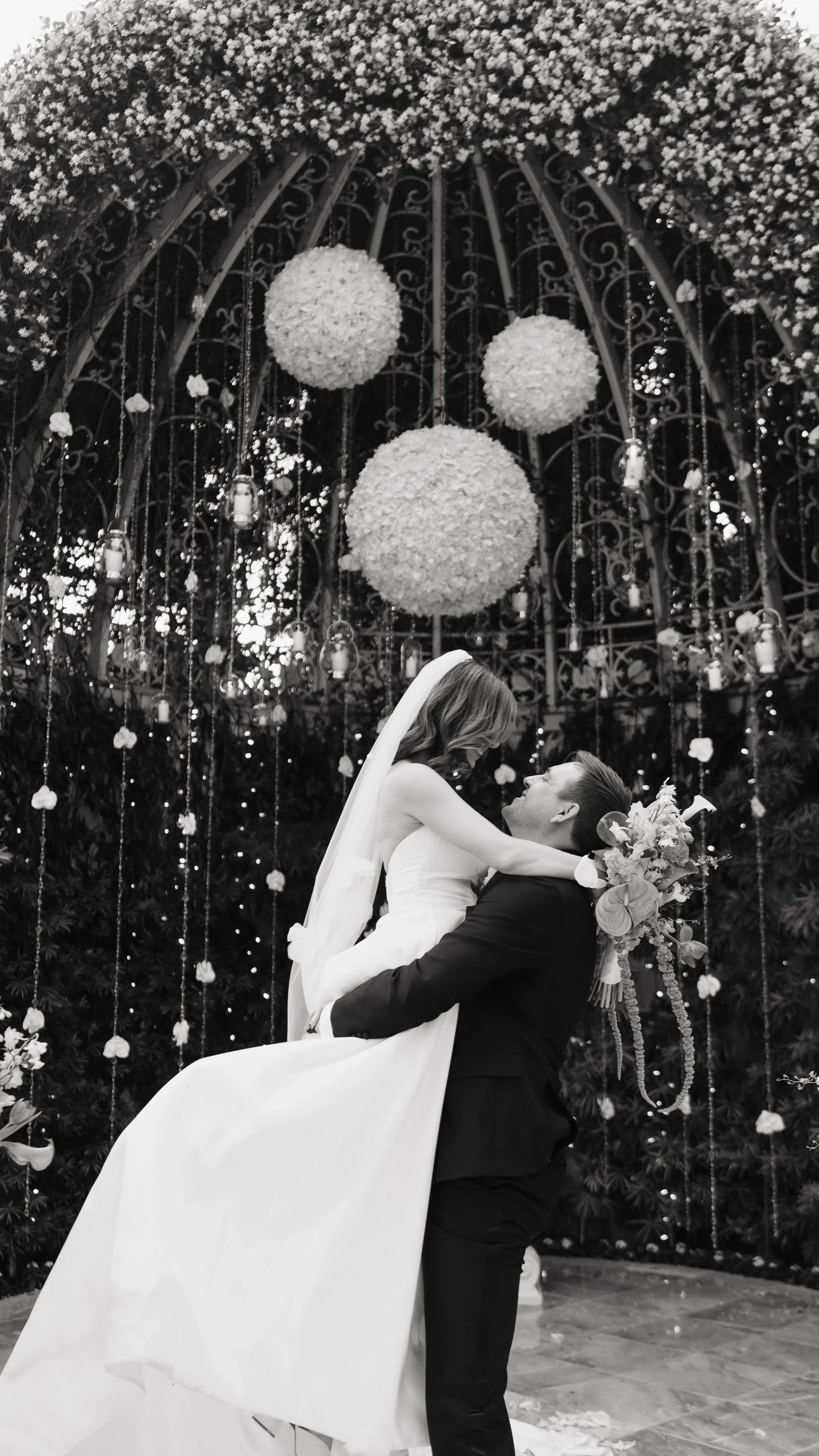 A bride and groom sharing a moment in front of a decorated wedding arch with hanging lanterns and floral arrangements.