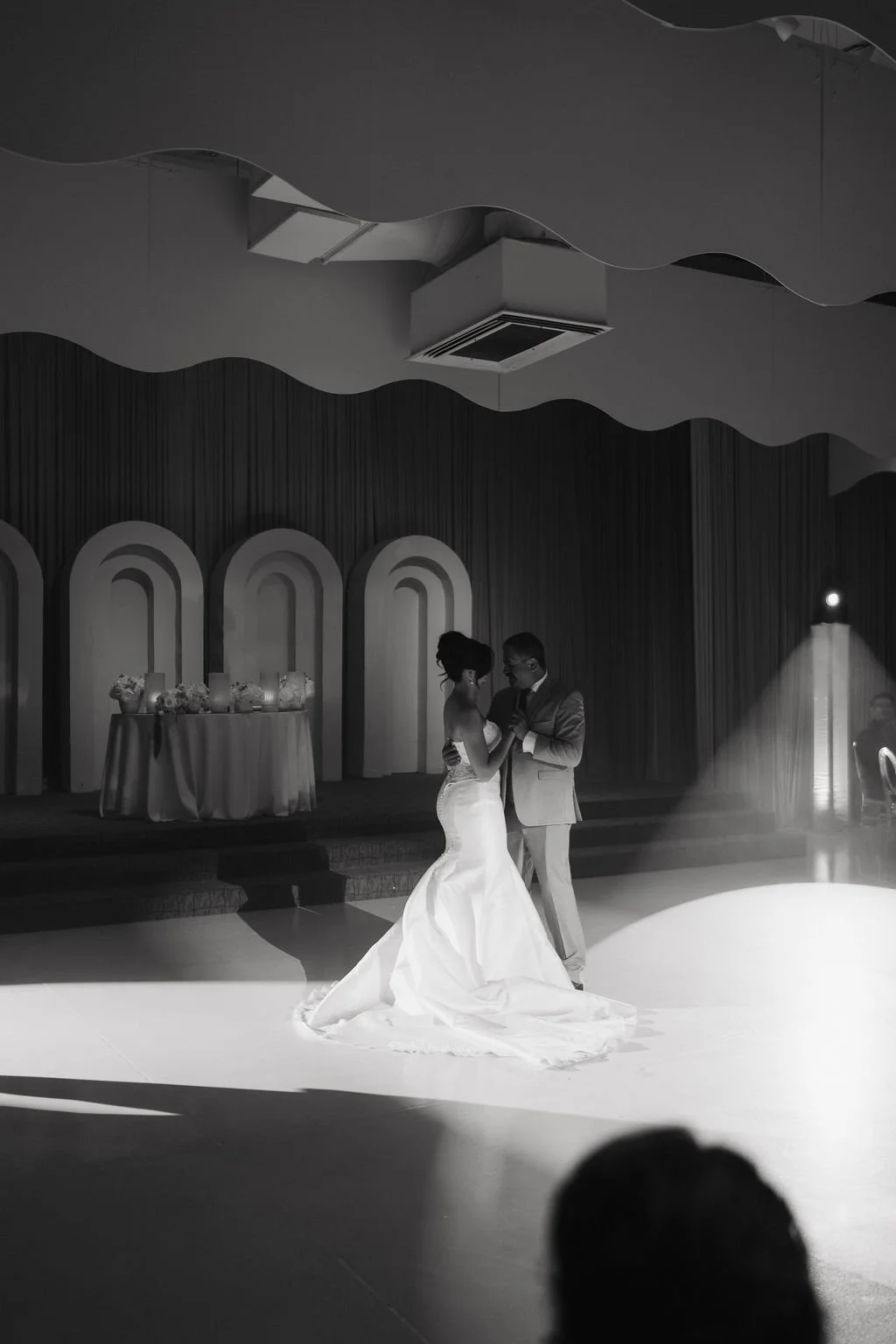 Bride and groom embracing beneath a spotlight during their romantic first dance.