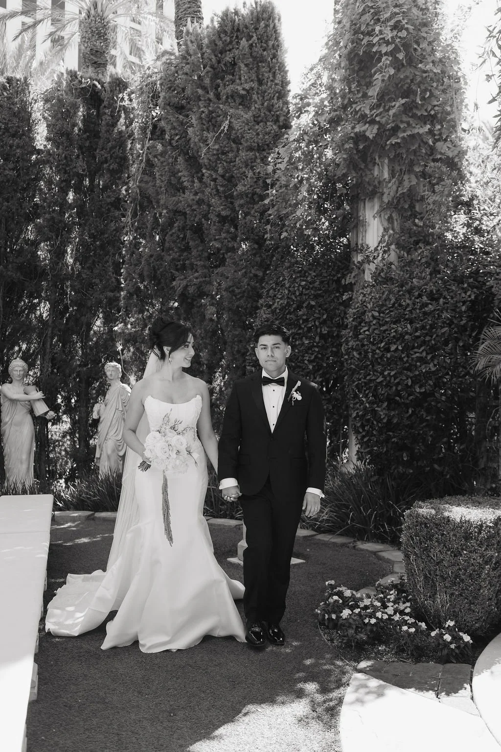 Bride and groom walking hand in hand through the sunlit garden of their Las Vegas wedding venue.