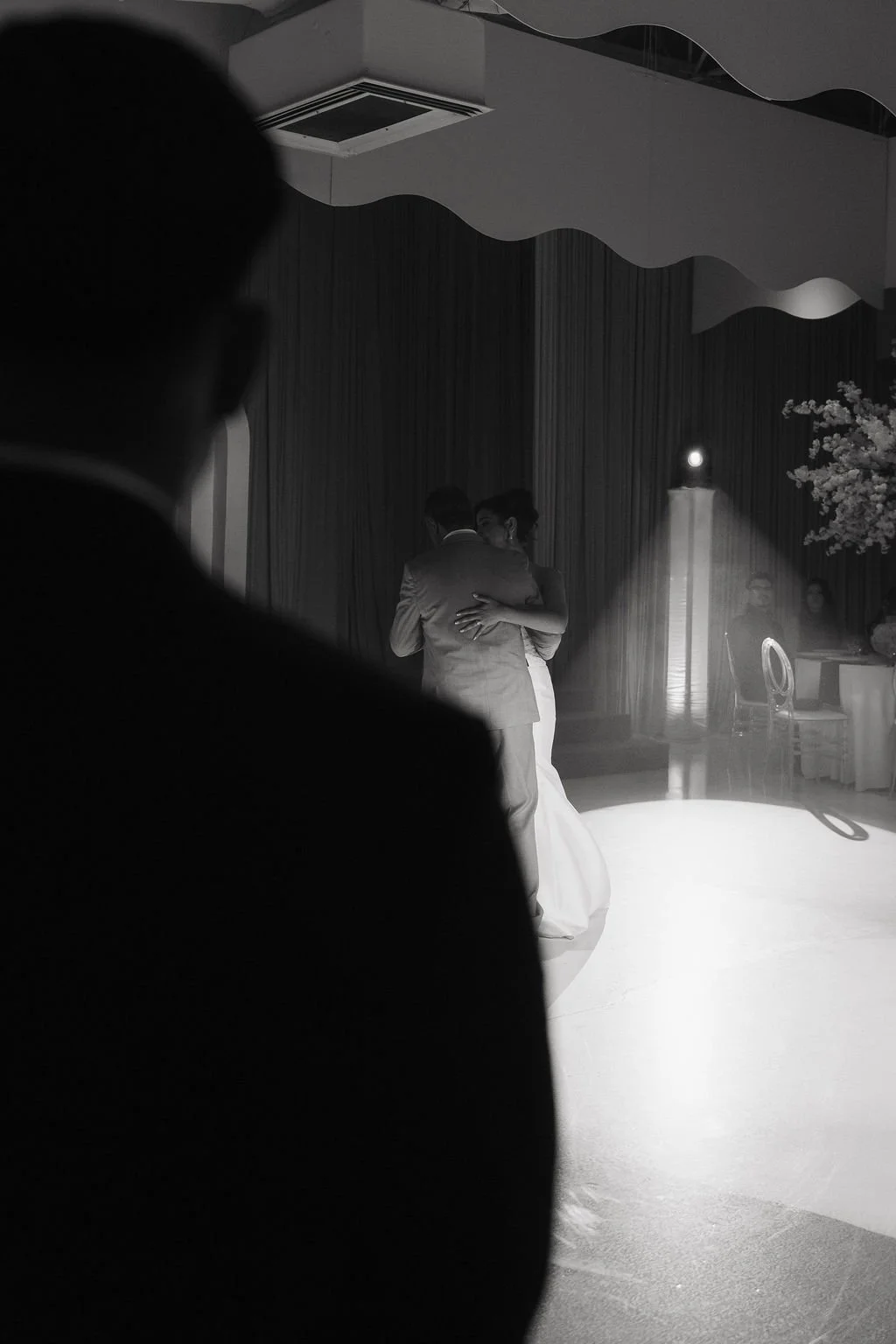 Black-and-white photograph of newlyweds sharing their first dance at an elegant wedding reception.