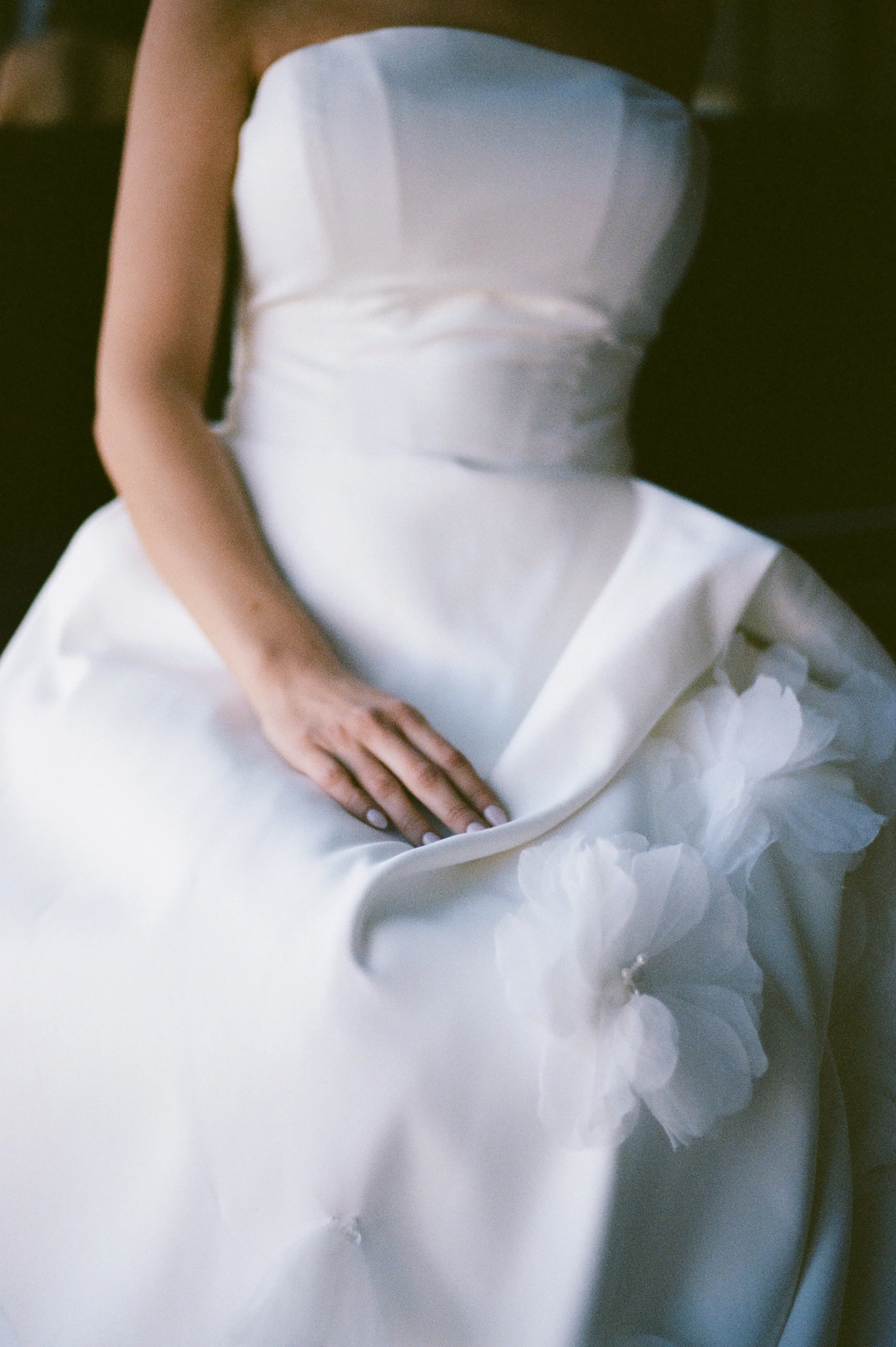 A bride in a white wedding dress with a strapless bodice sitting with her hand resting on her lap.