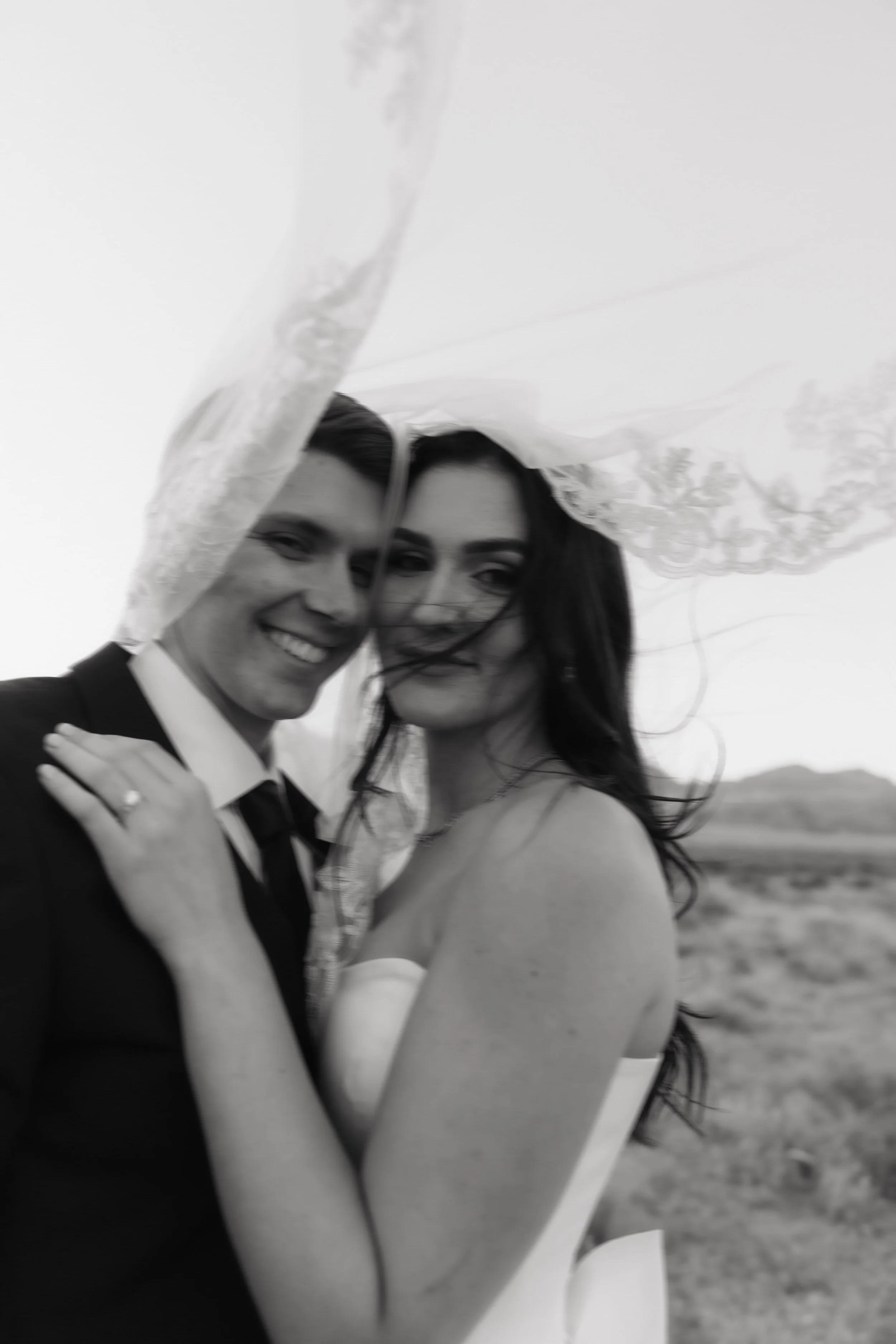 Editorial shot of bride and groom with bride's veil flying over them