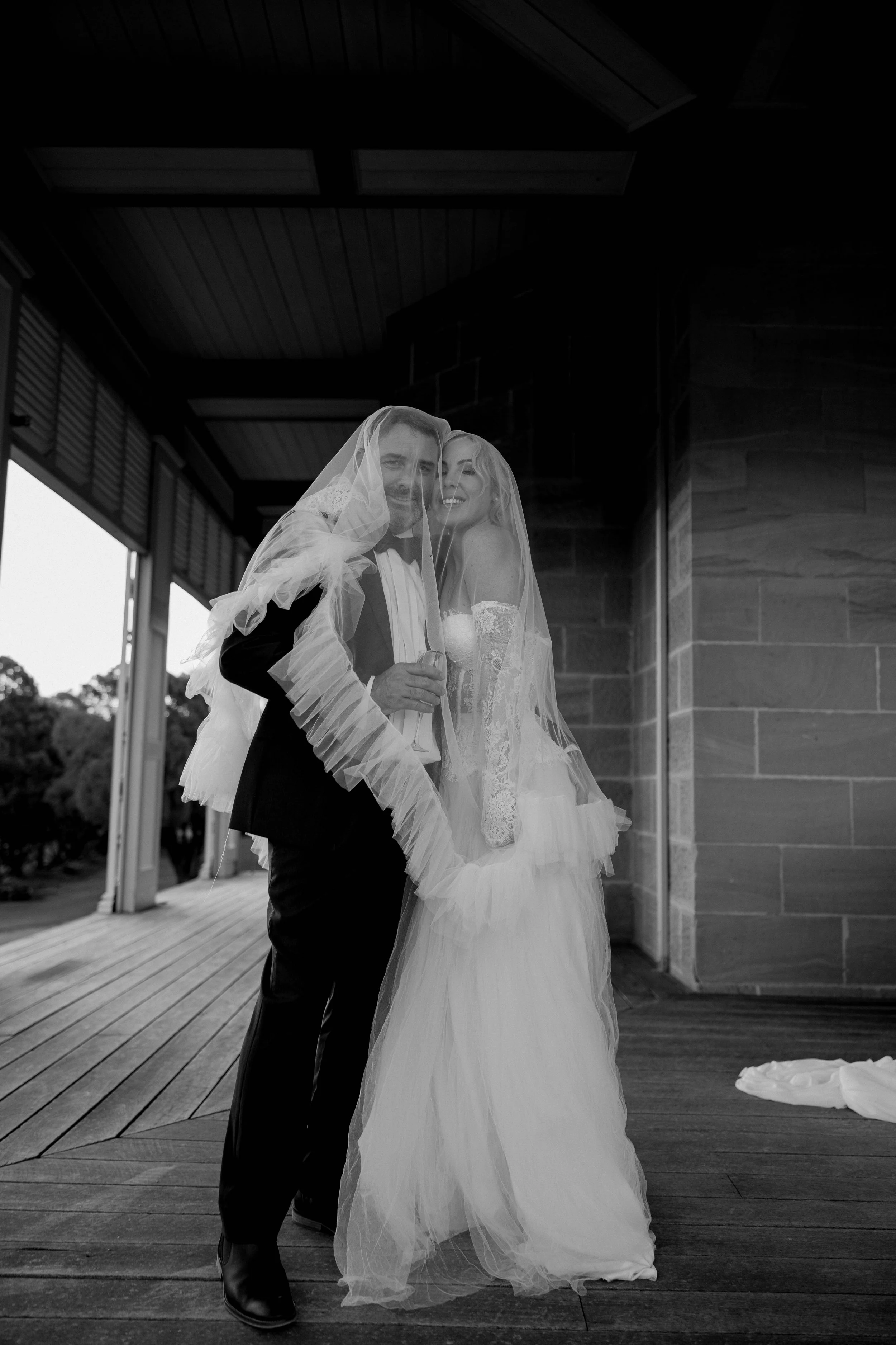 A bride and groom smiling between each other inside a building with wooden flooring and walls, and large windows. Brisbane wedding photographer 