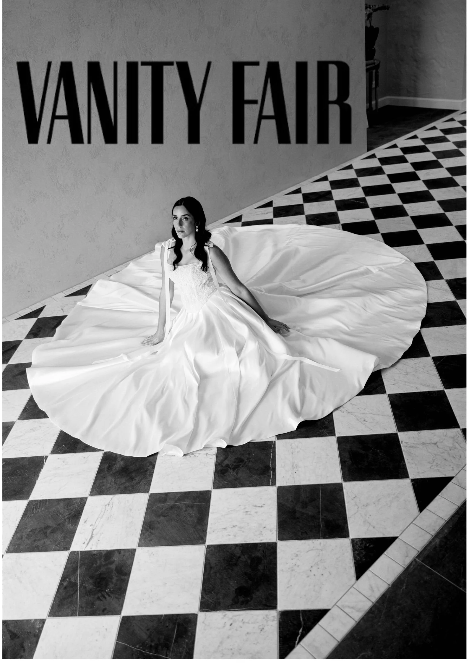 Black and white photo of a woman in a white gown sitting on a checkered floor in front of a wall with a Vanity Fair sign.