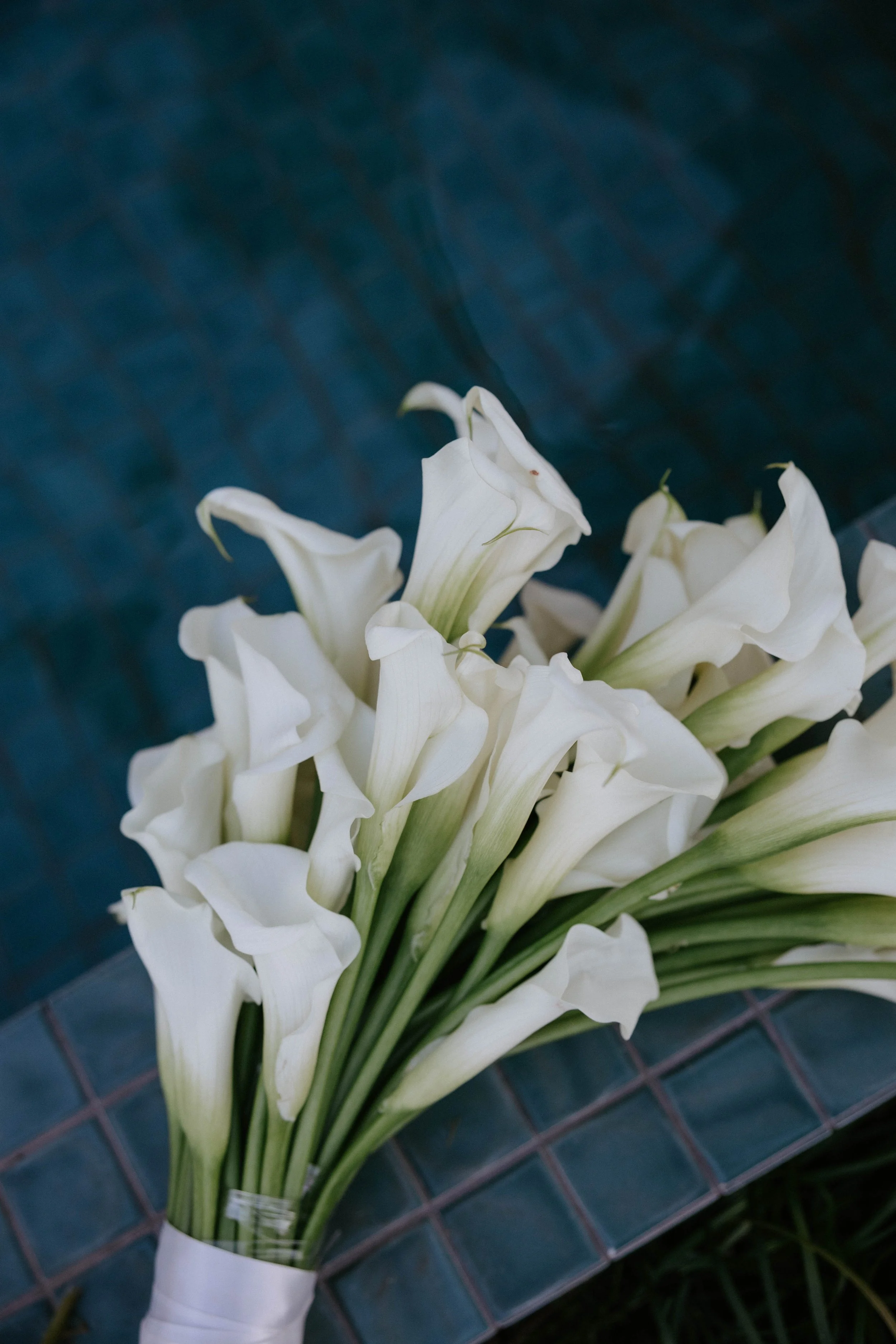 White calla lily flowers in a bouquet on a dark tiled surface.
