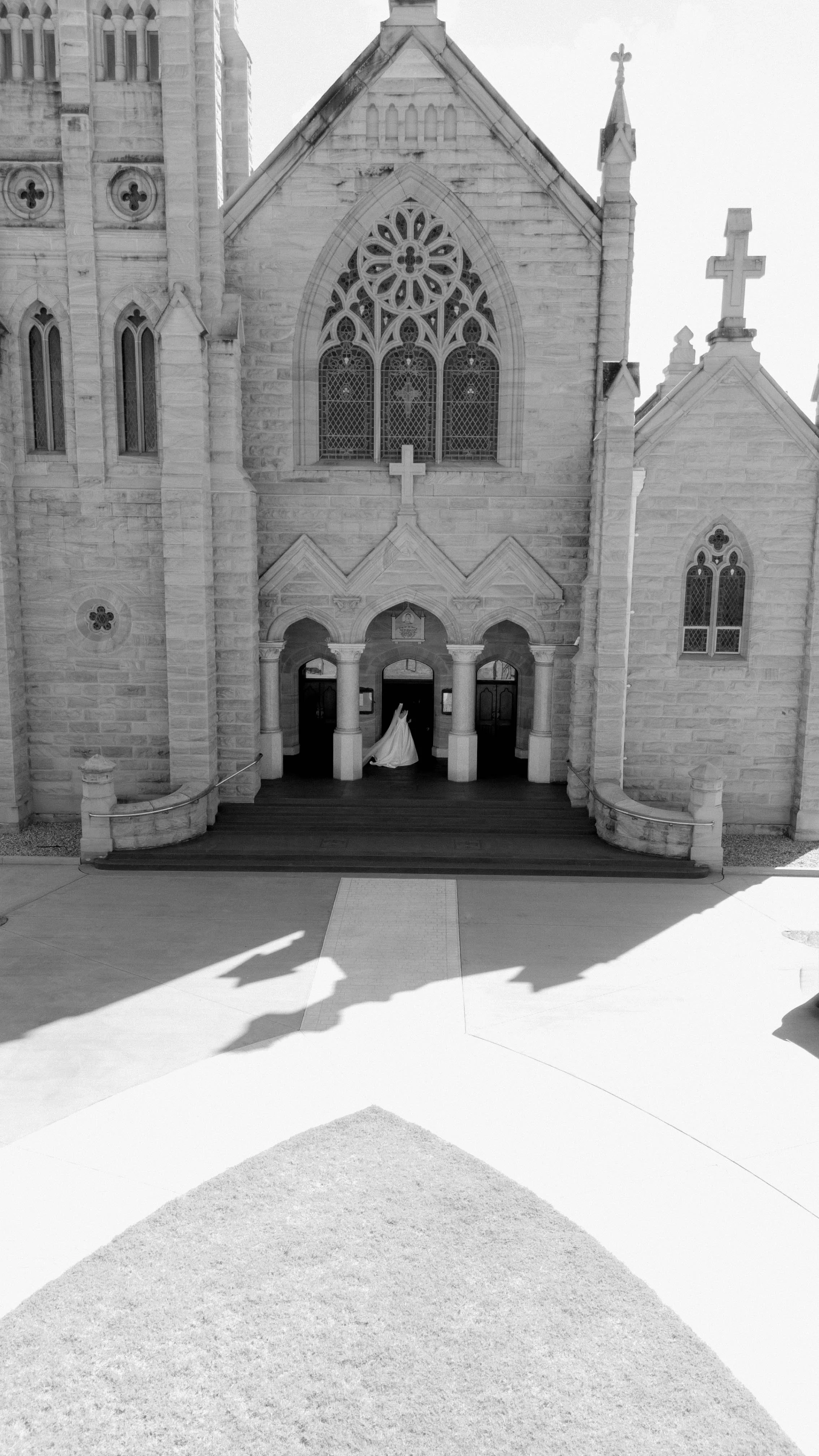 Front view of a Gothic-style church with stained glass windows and a small bride in a white wedding dress and veil walking inside.