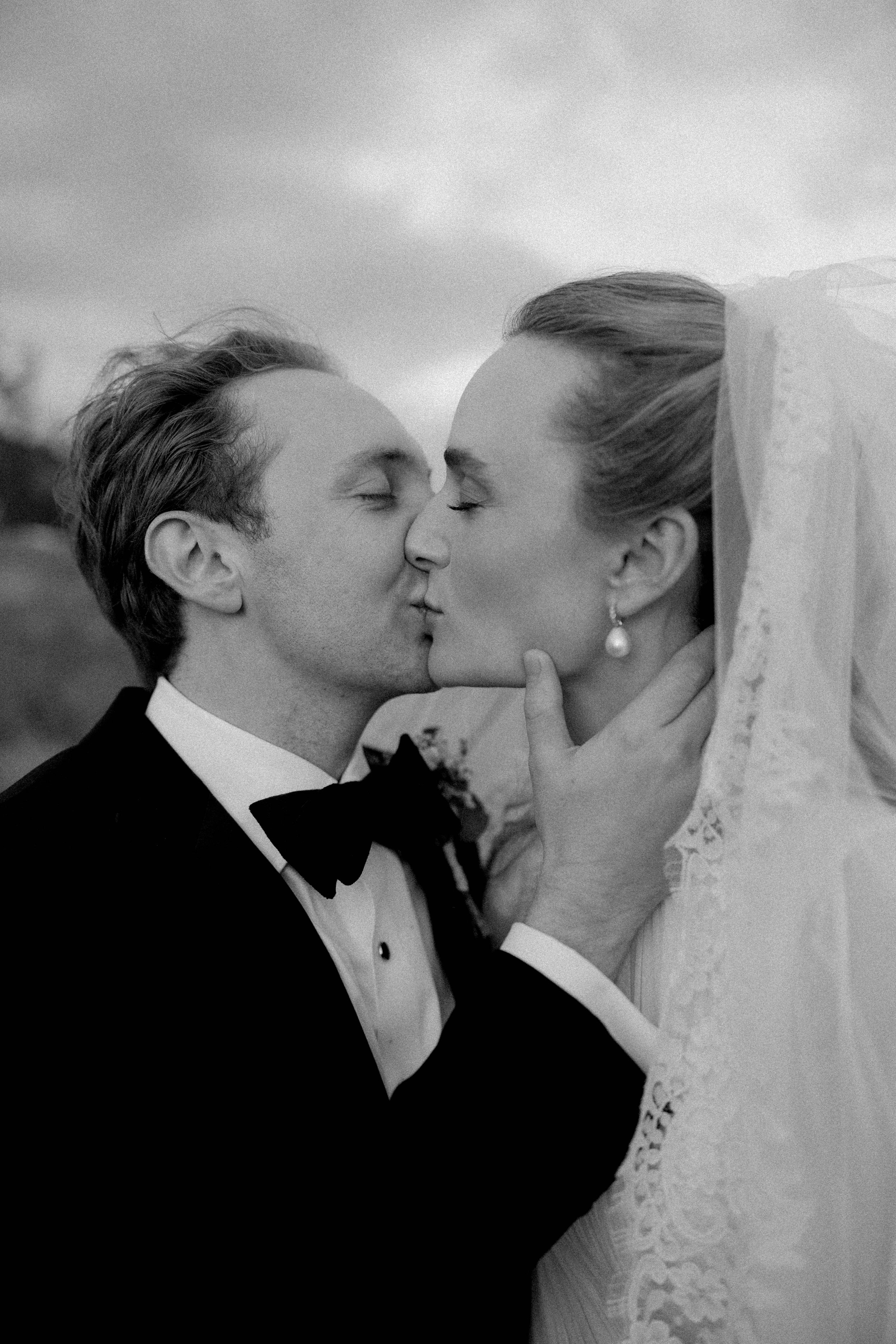 A black-and-white photo of a wedding couple, with the bride and groom touching noses and eyes closed, in an intimate moment.