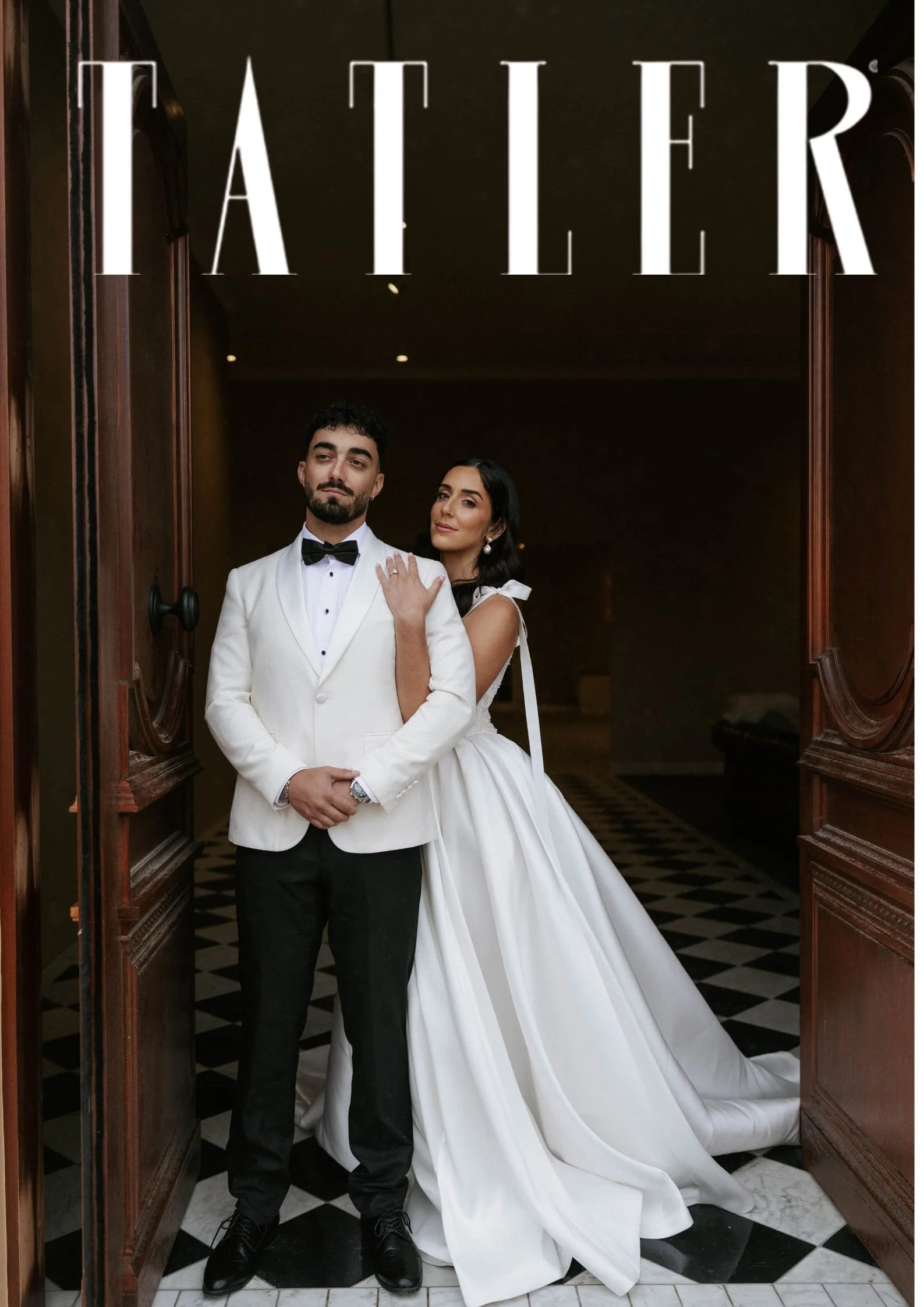 A bride and groom in wedding attire standing in a doorway with wooden framing at a wedding or formal event.