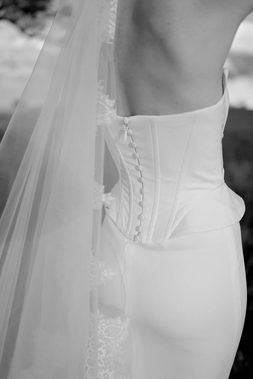 Close-up of a bride's wedding dress, focusing on the side with a series of fabric-covered buttons and a sheer veil.