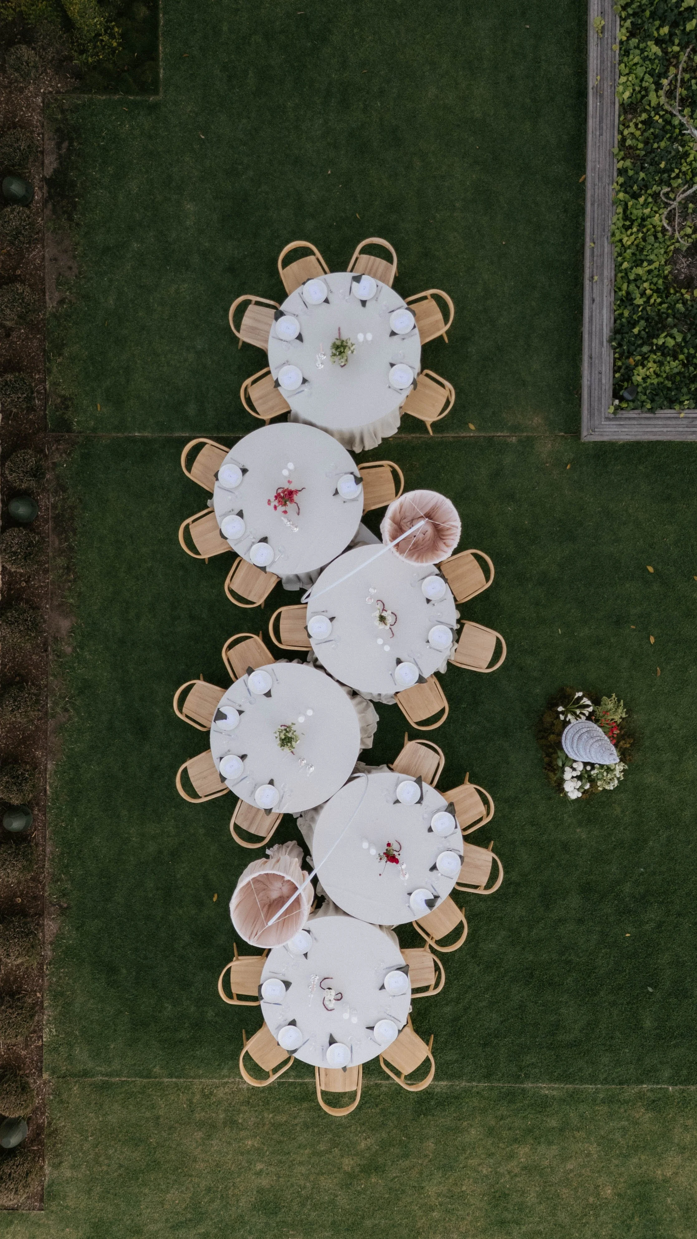 Overhead view of several round banquet tables with white tablecloths and wooden chairs set up on a grassy outdoor area, decorated with floral centerpieces and white plates. The dairy Ravensbourne toowooomba 