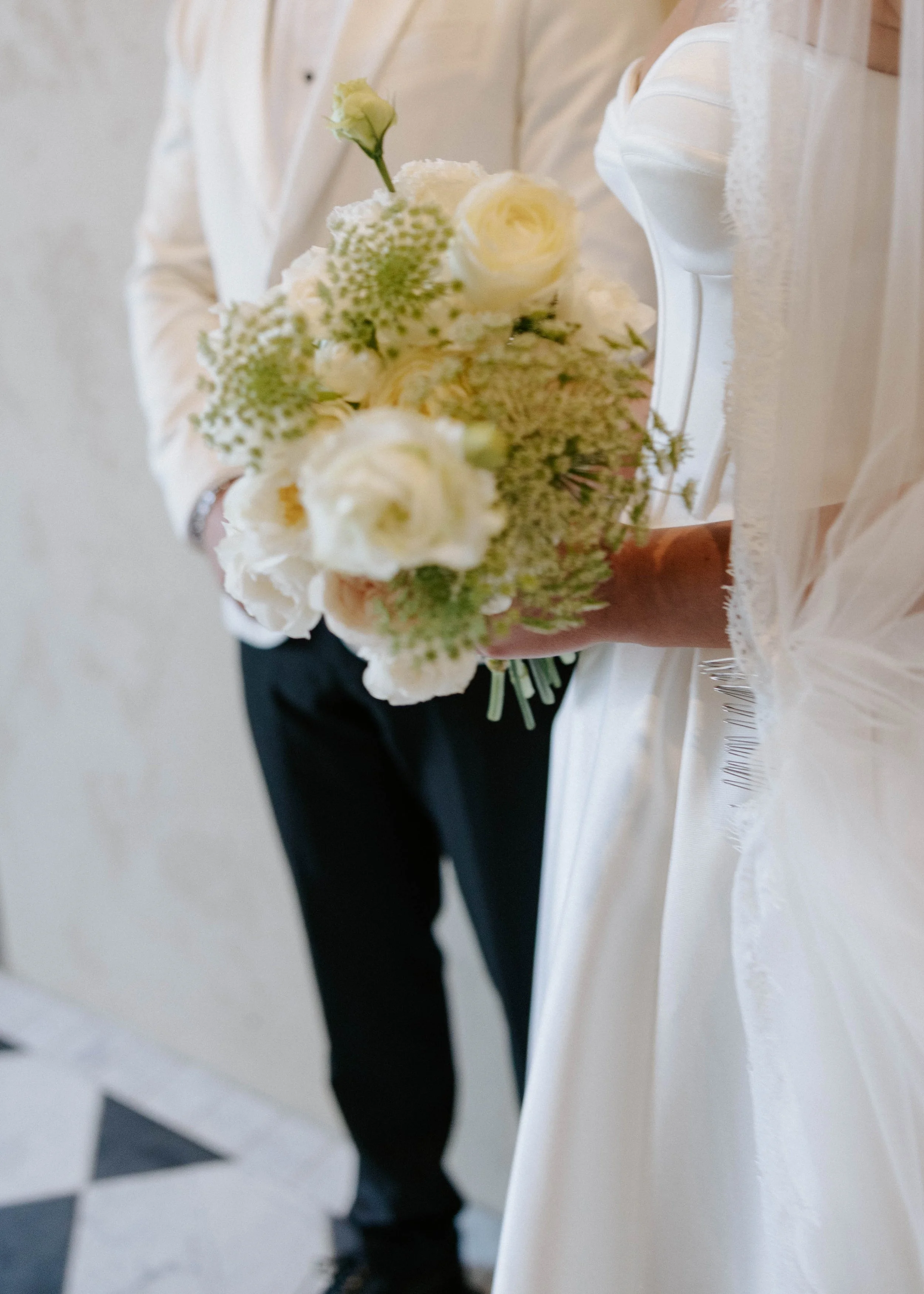 Person holding a small bouquet of white and cream flowers with lace details on the clothing.