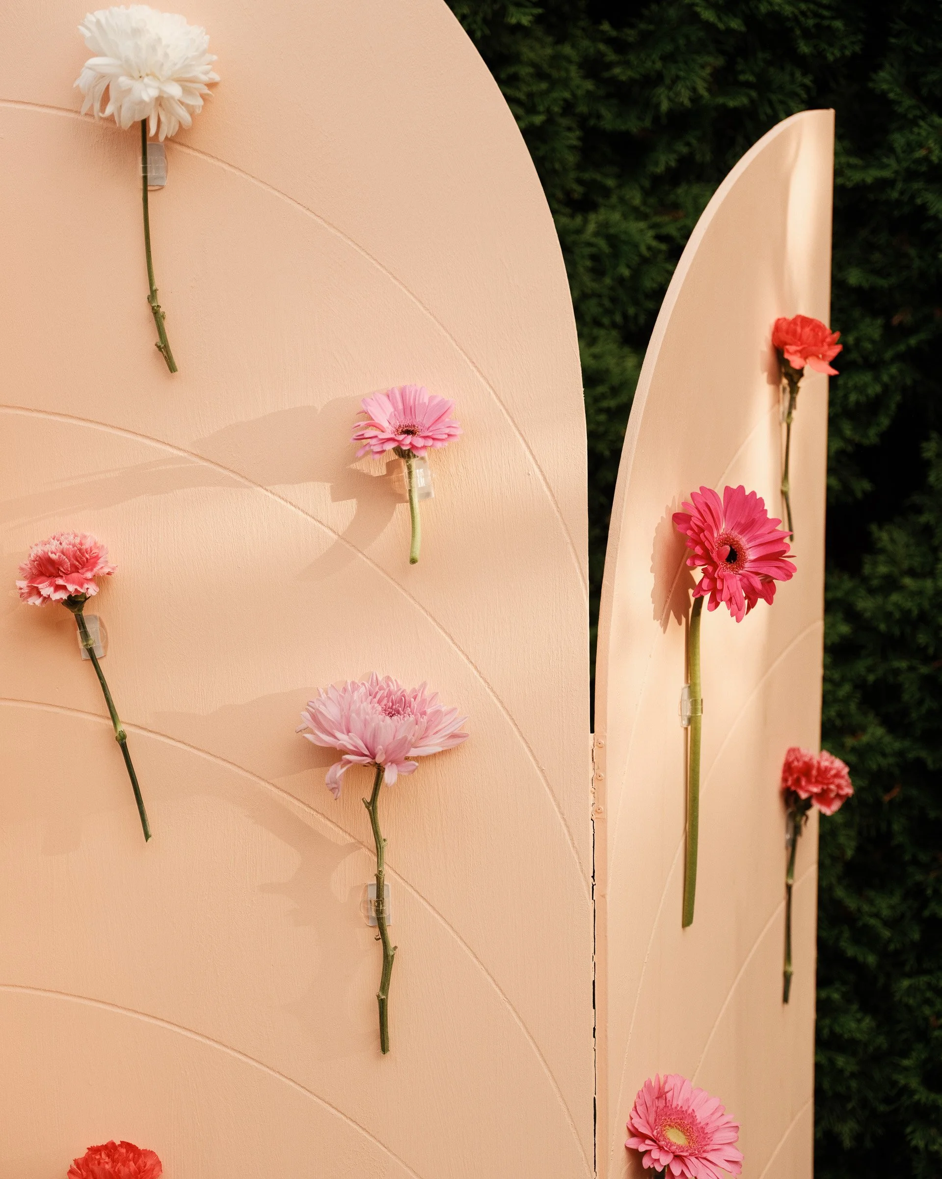 Pink panels with pink and white flowers attached, arranged vertically against a background of green foliage.