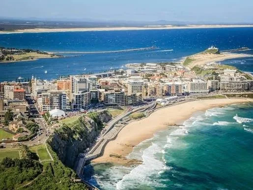Aerial view of a coastal city with high-rise buildings, a sandy beach, and a large body of water in the background.