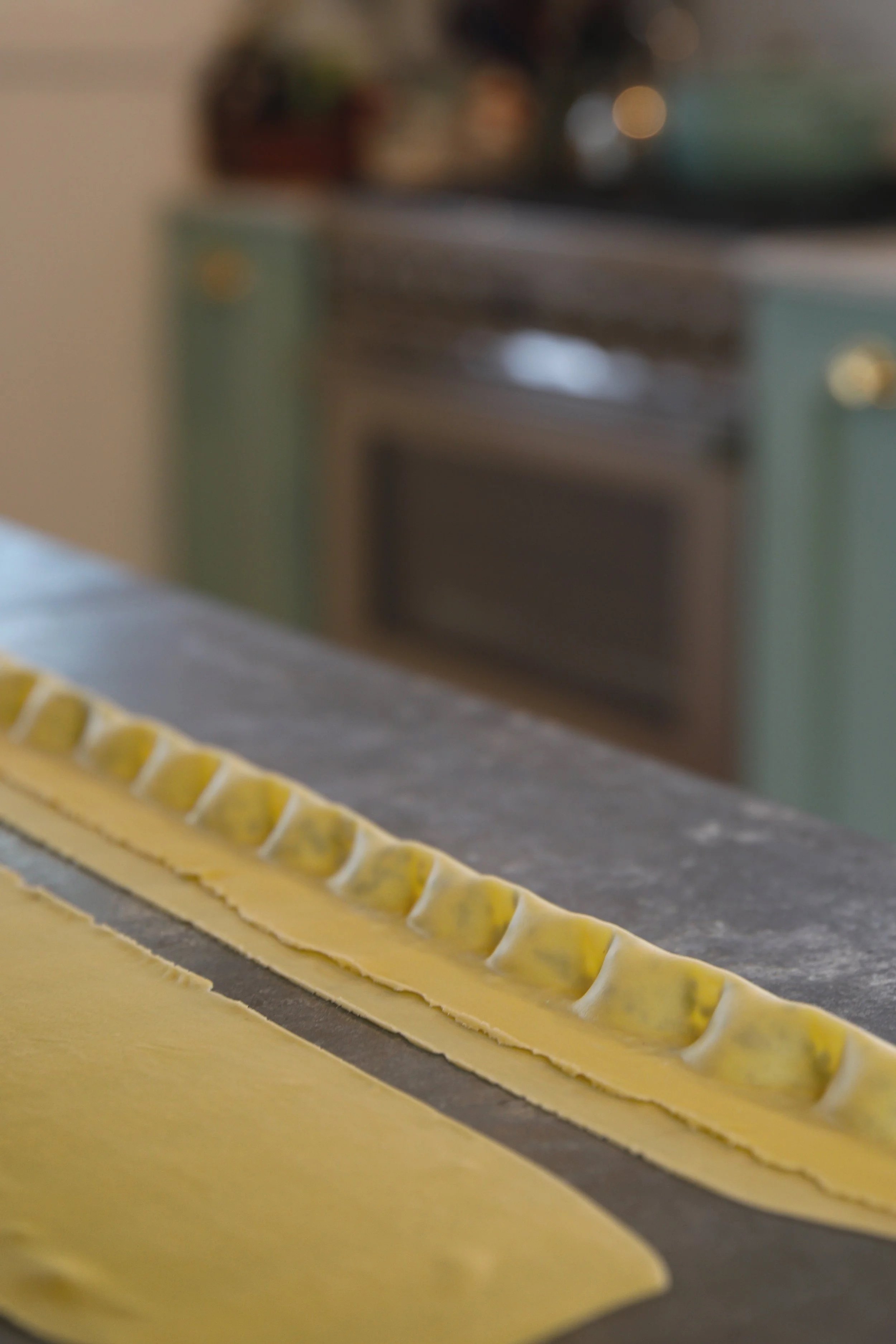Close-up of hand made Italian pasta being filled and shaped into agnolotti on a counter in a kitchen.
