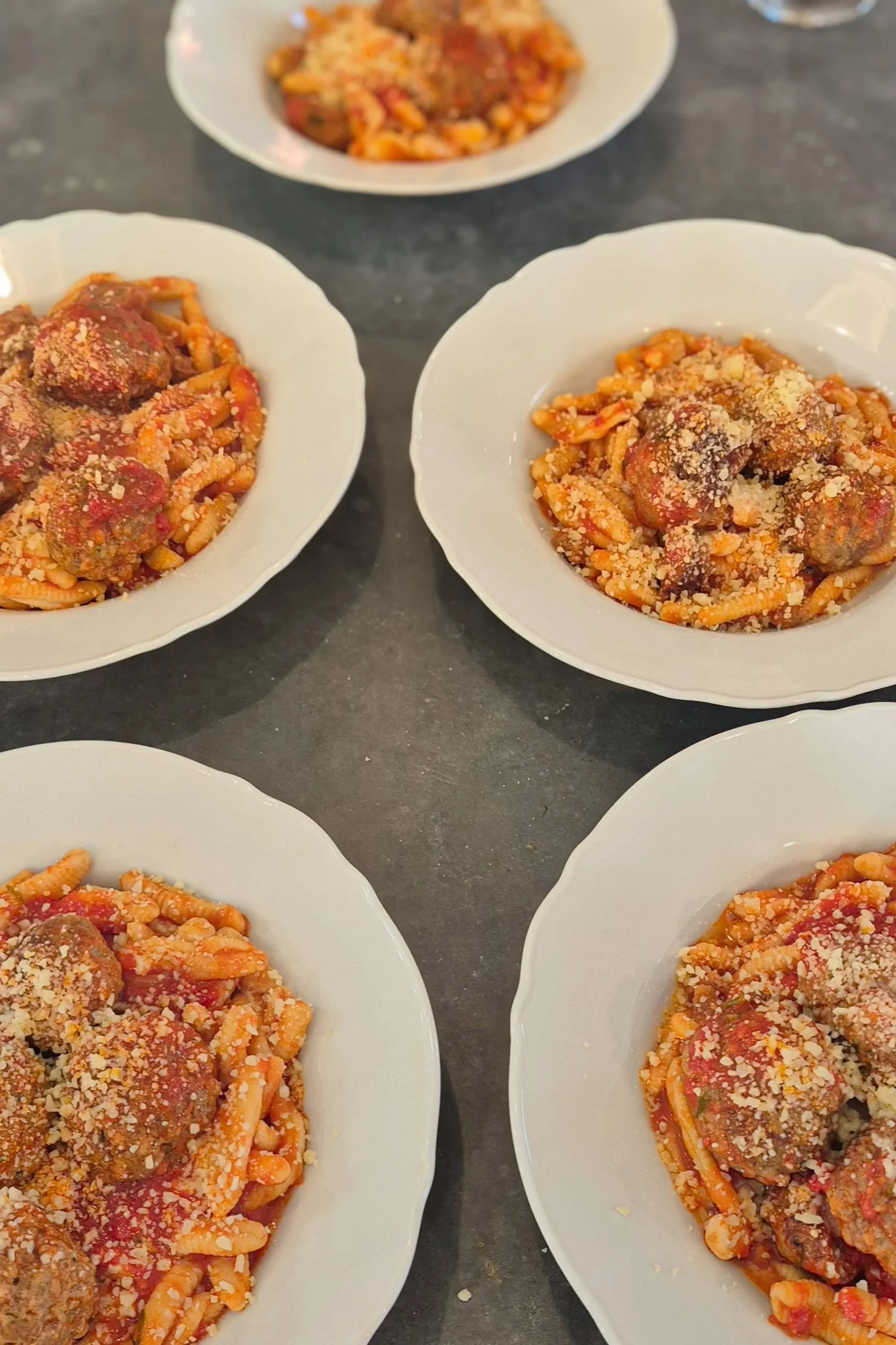 Several white bowls filled with hand rolled semolina pasta and meatballs topped with tomato sauce and grated cheese