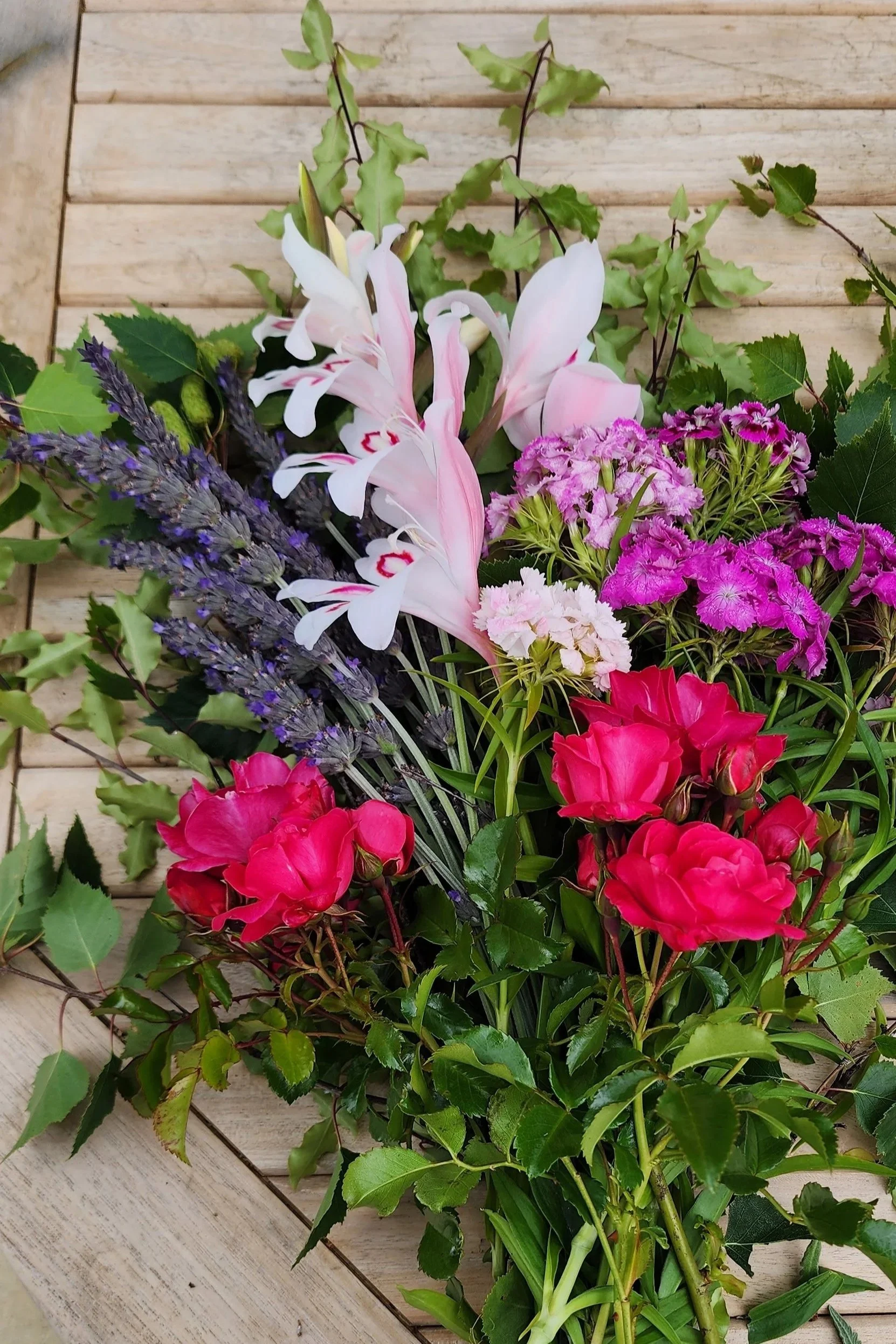A bouquet of pink and purple flowers with green leaves on a wooden surface.