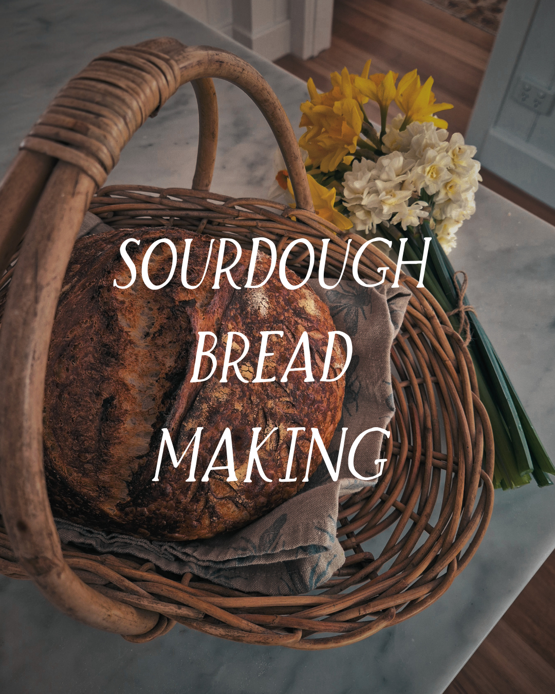 Sourdough bread in a wicker basket with flowers nearby.
