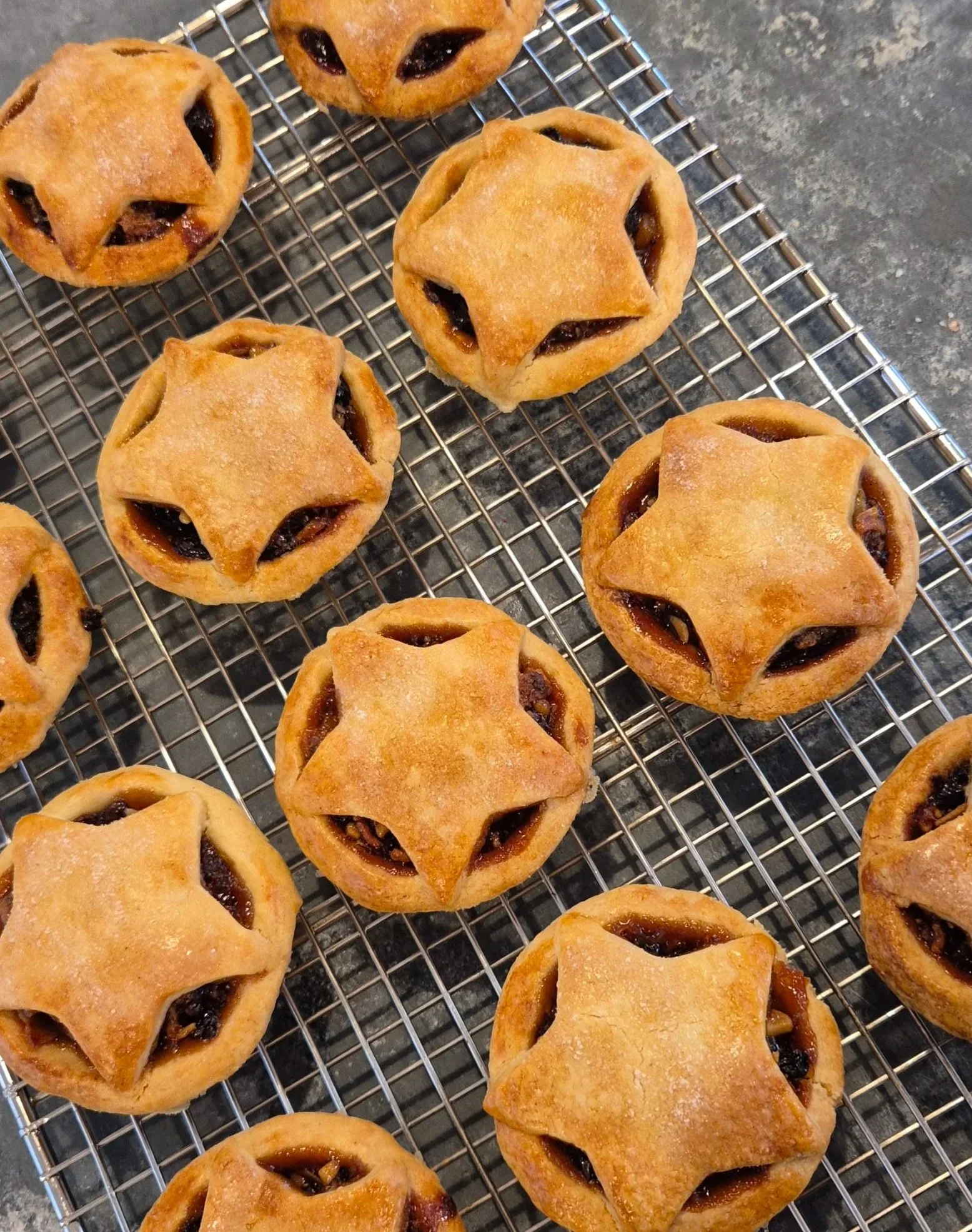 Freshly baked fruit mince pies with star-shaped pastry lids, cooling on a wire rack.
