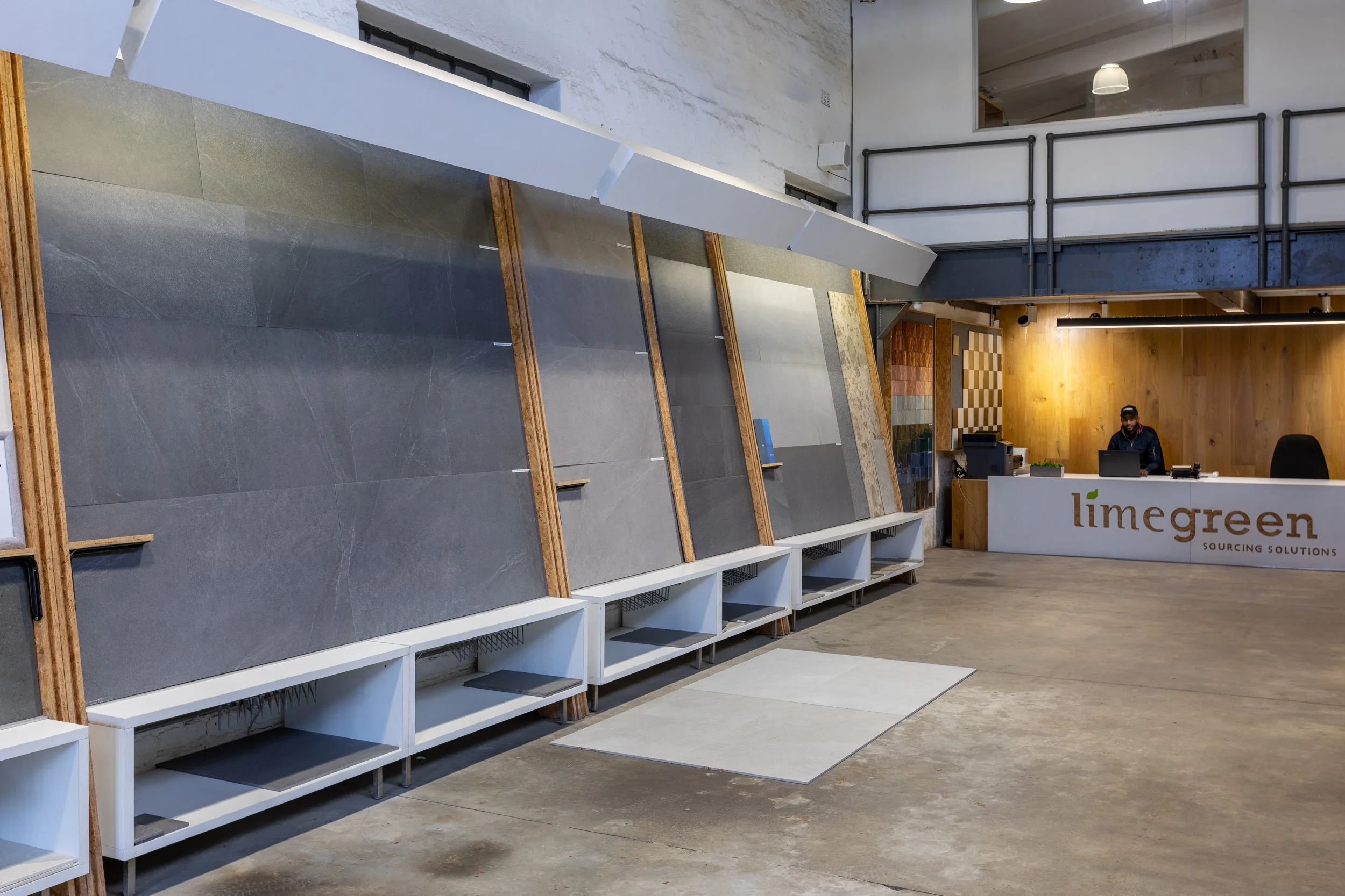 Display of large tiles and flooring materials at Lime Green Sourcing Solutions showroom with a sales counter and a person working.