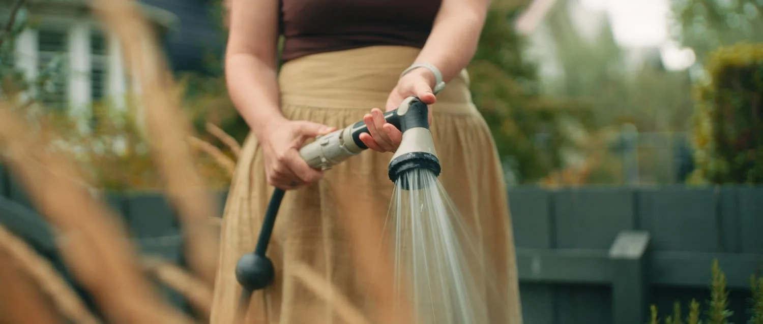 Film still from Things Will Be Different, showing a person watering plants in a garden with a hose.