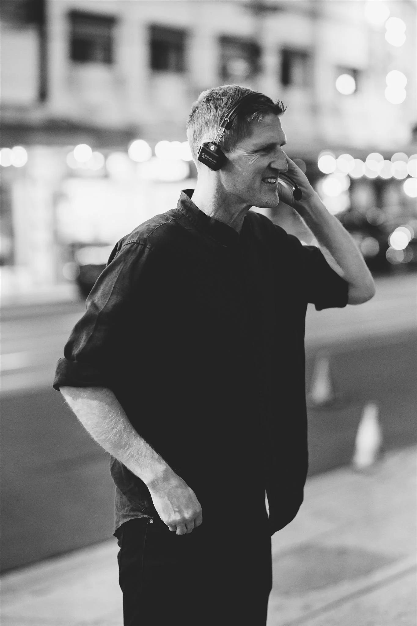 Behind-the-scenes portrait of Jerome Cole smiling on set at night, wearing a production headset with city lights in the background.
