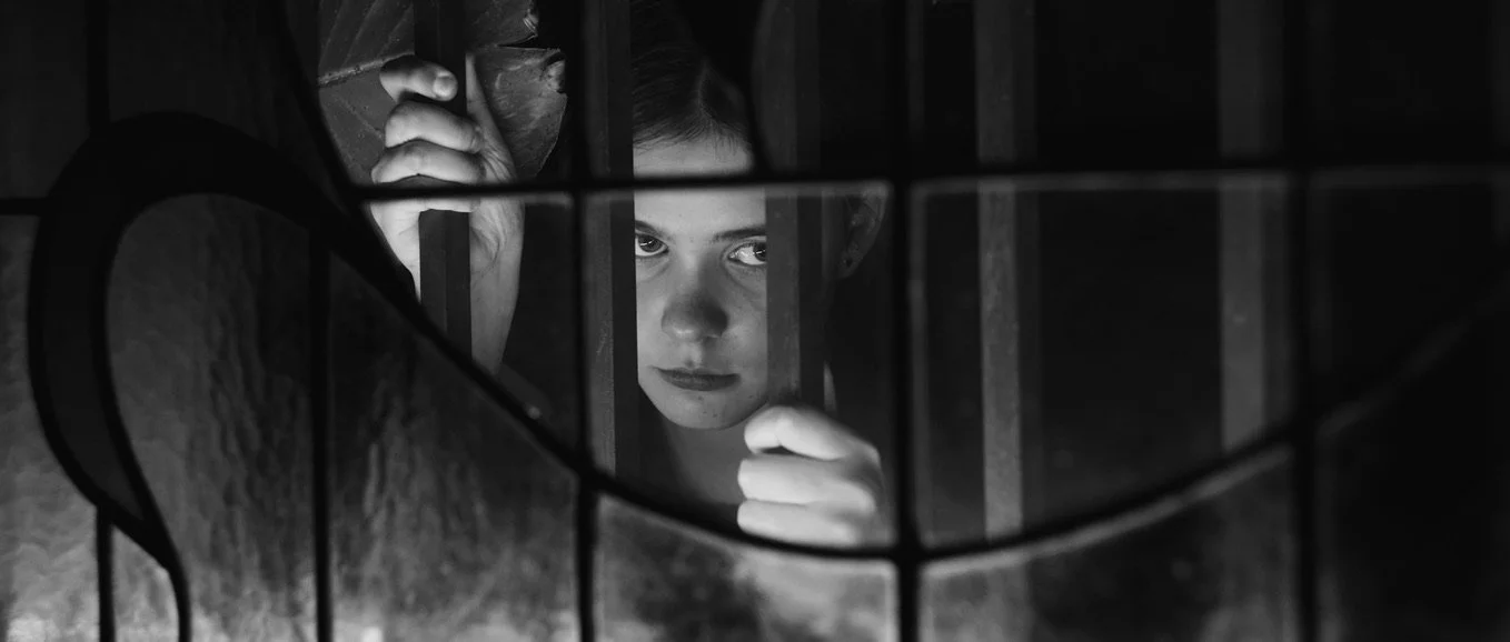 Film still from Cugini, showing a person with a serious expression seen through the bars of a jail cell.