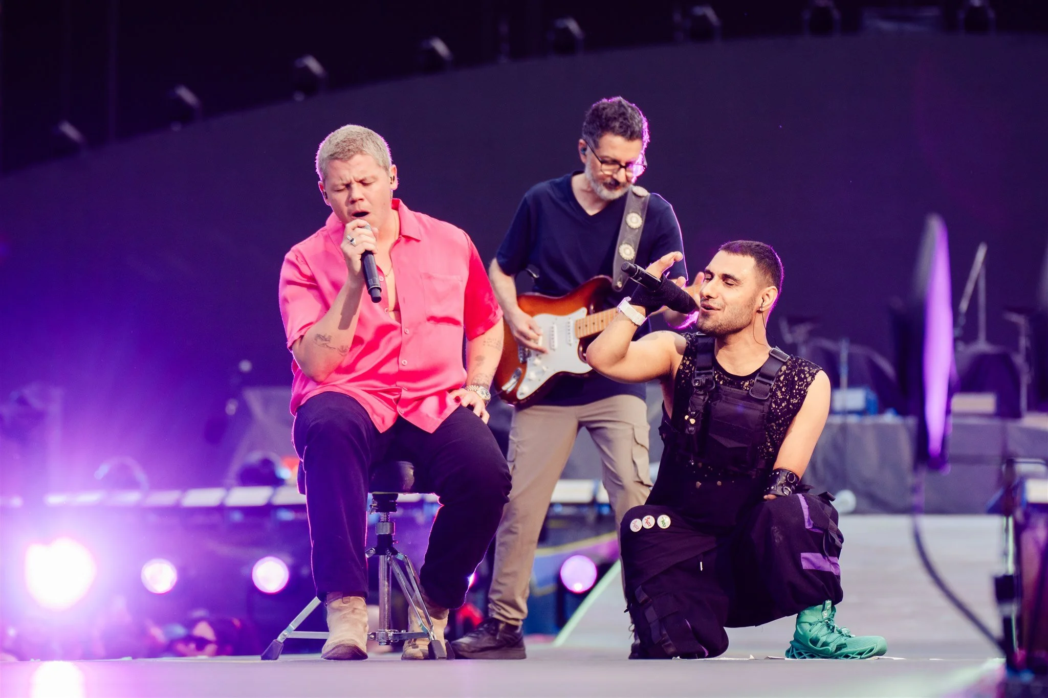 Emmanuel Kelly performing on stage with his band under purple stage lighting.