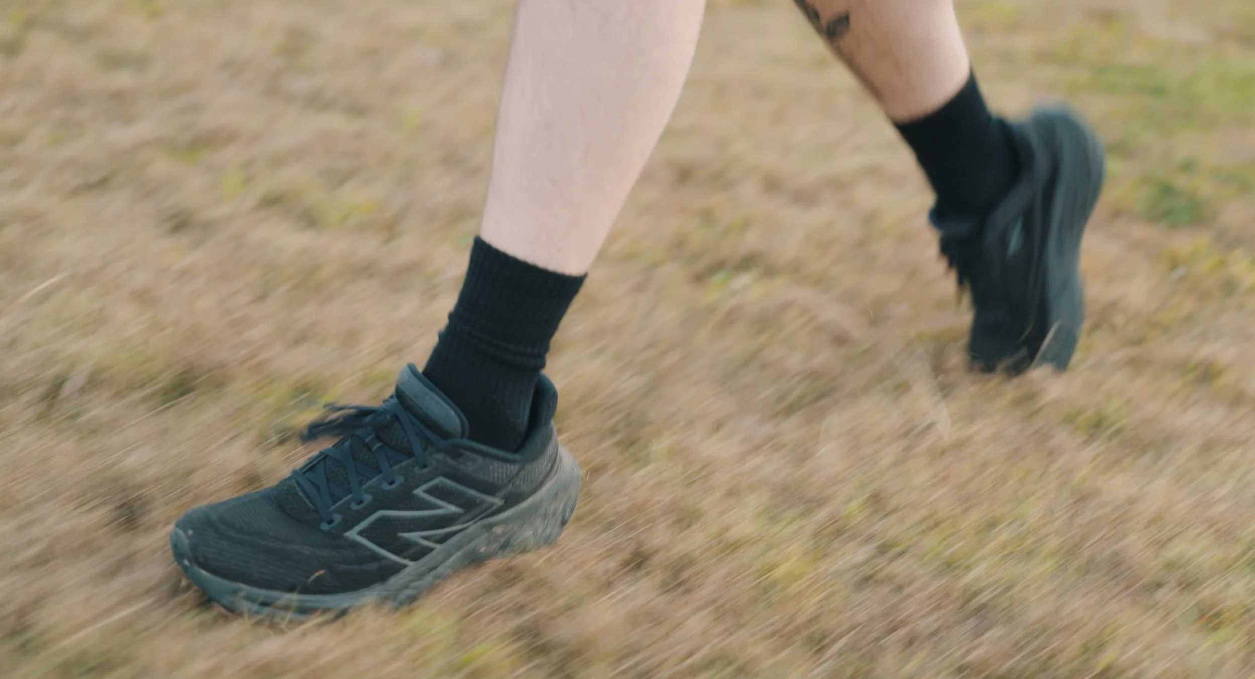 Close-up of a person's legs wearing black socks and black running shoes while running outdoors on a grassy surface.