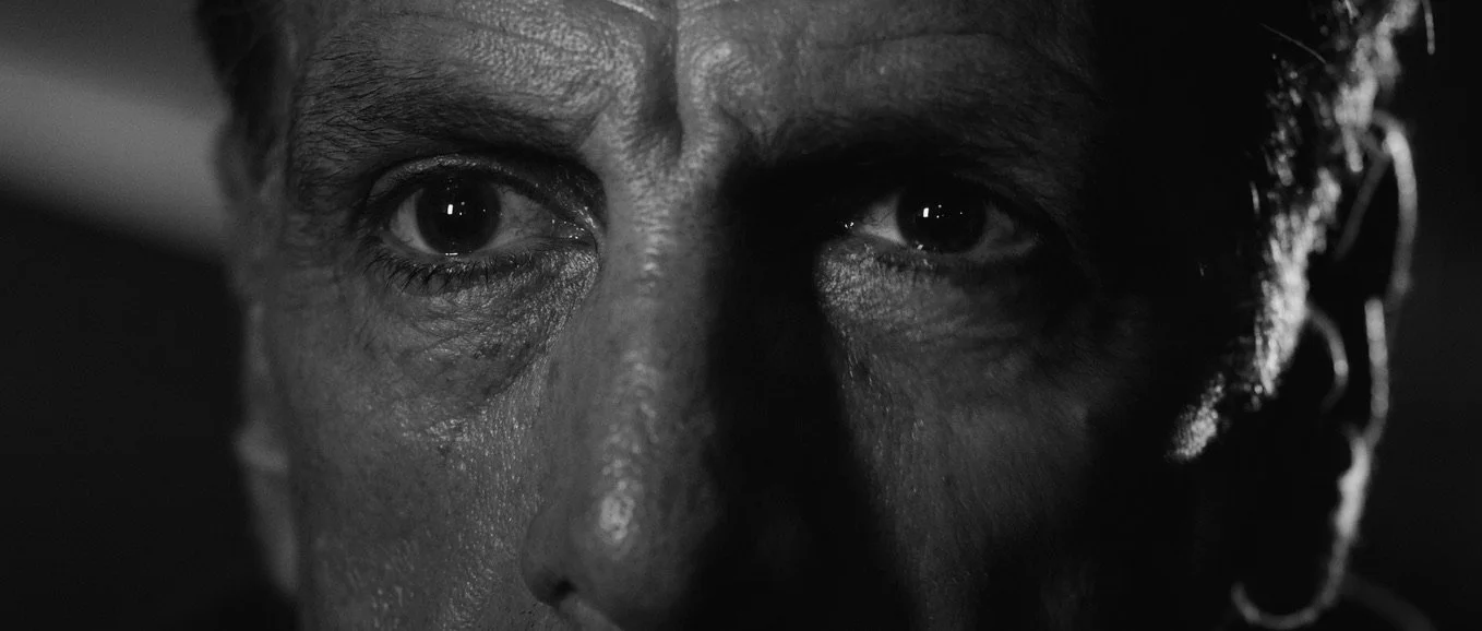 Film still from Cugini, showing a close-up black-and-white portrait of a man with an intense expression.