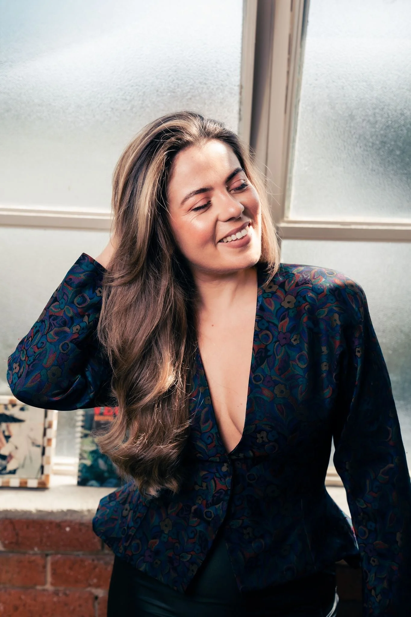 Portrait of Lauren Acciarito, founder and fashion designer of ACCI, smiling in her studio beside a frosted window and brick wall.
