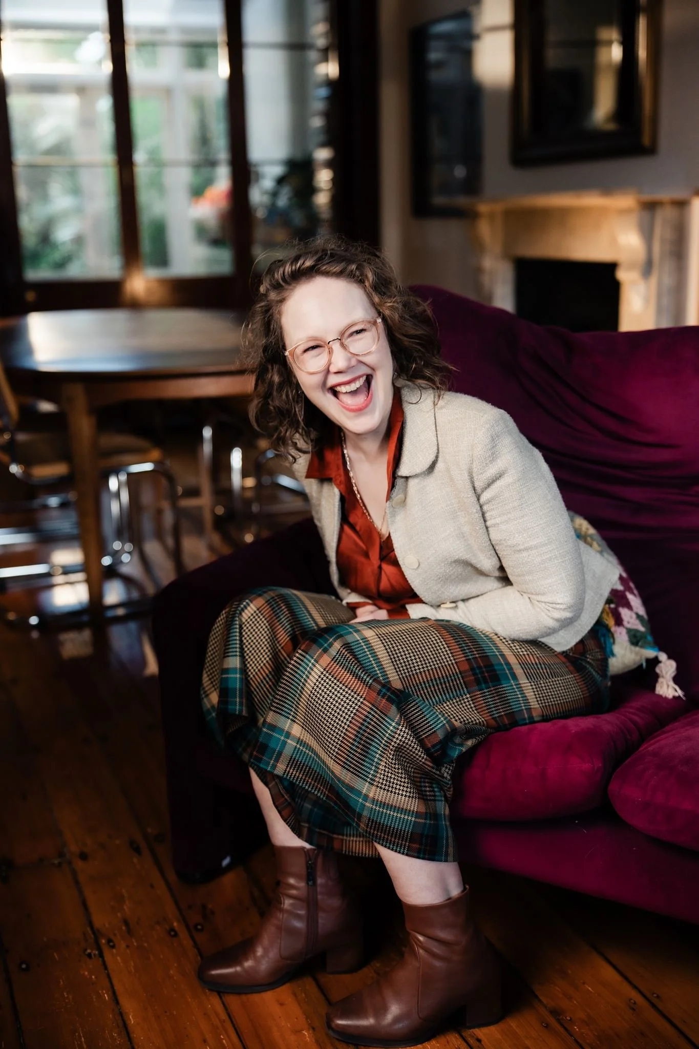 Portrait of Mary Un from Anglican Deaconess Ministries, smiling on a red velvet couch in a light-filled room.