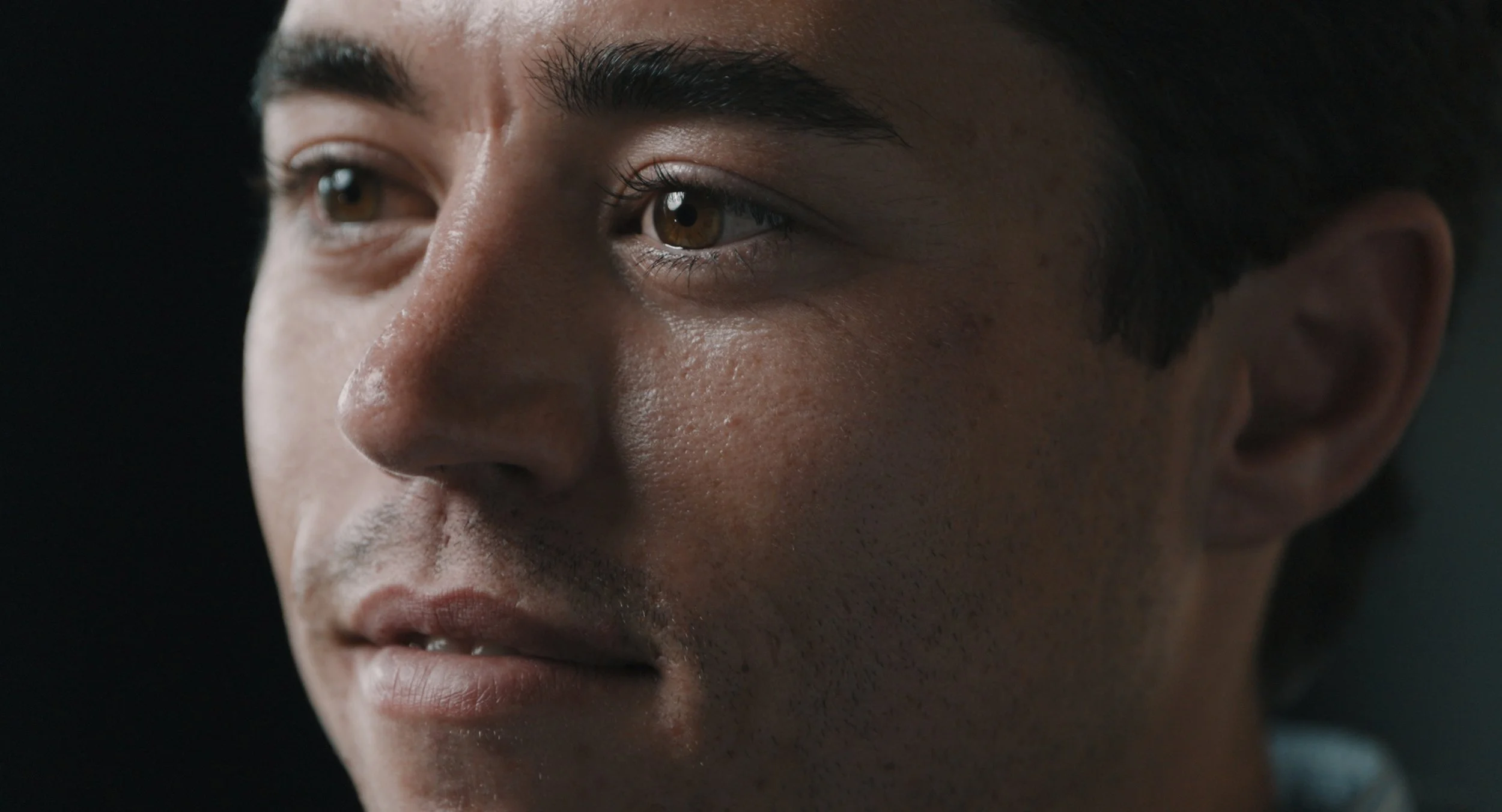 Close-up of a person's face with dark hair, brown eyes, and smooth skin.