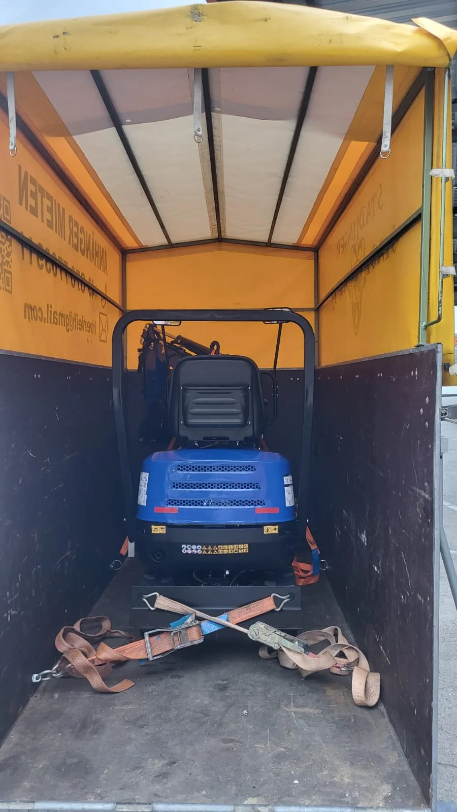Ein blauer Kompaktroller in einem gelben Transporter mit schwarzem Boden und karminroten Sicherheitsgurten befestigt.