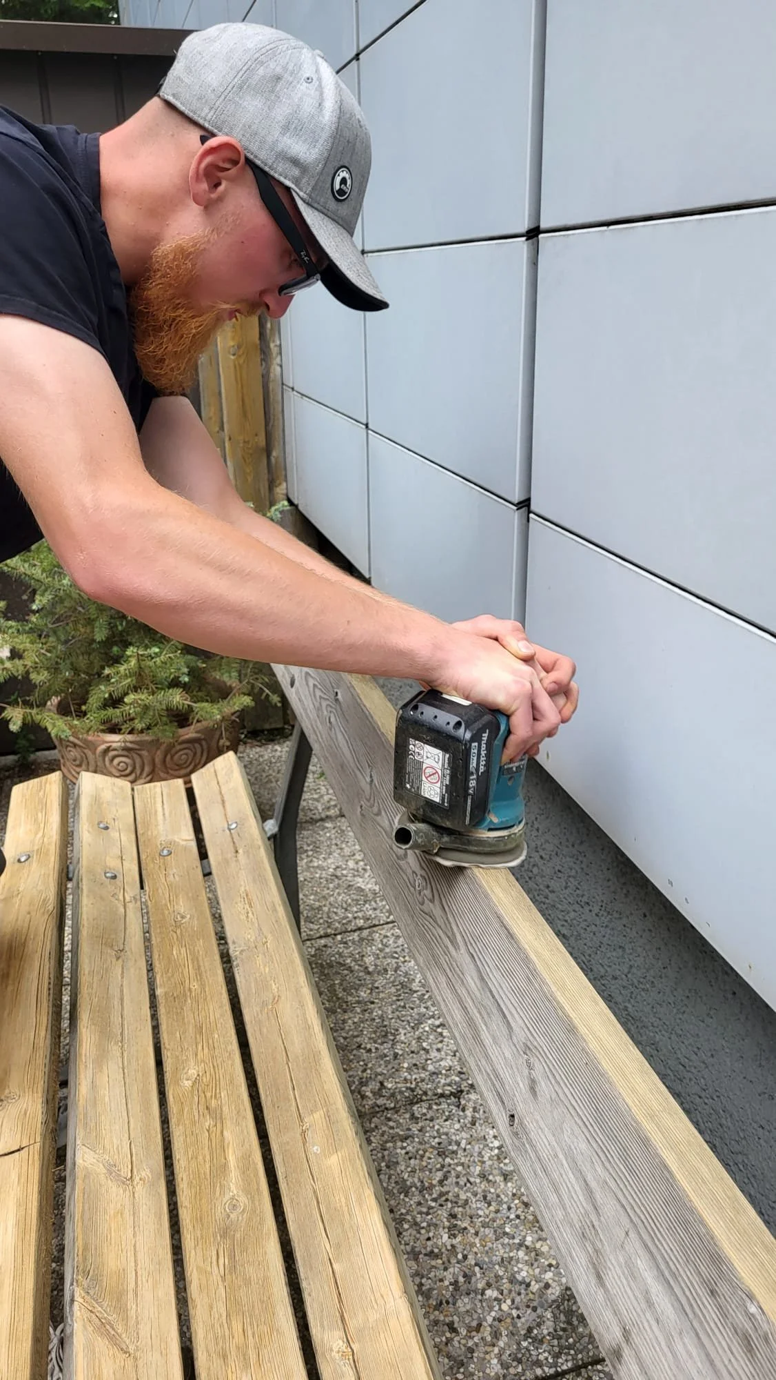 Ein Mann bearbeitet Holz mit einem Elektrowerkzeug im Freien.