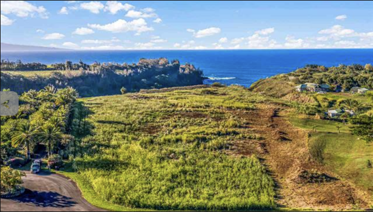 Scenic landscape with rolling green hills, scattered trees, and distant cliffs meeting the ocean under a partly cloudy sky.