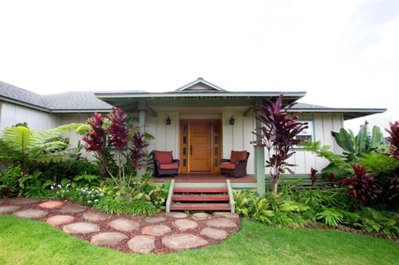 Front view of a house with a front porch, two chairs, and a garden with various plants and shrubs.