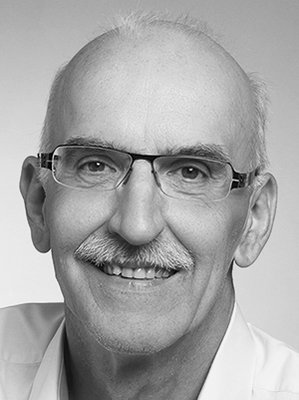 Schwarz-weiße Nahaufnahme eines älteren Mannes mit Brille, weißen Haaren und Schnurrbart, lächelnd