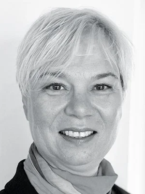 Schwarz-Weiß-Porträt einer Frau mit kurzer, blonder Frisur, lächelnd, vor neutralem Hintergrund.