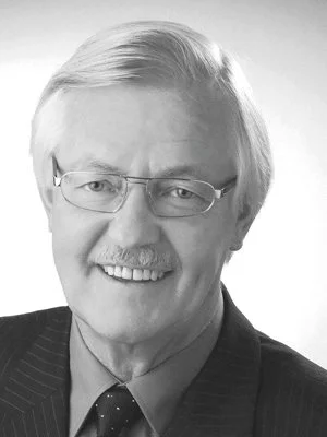 Schwarz-weiß Porträt eines älteren Mannes mit Brille, grauem Haar und einem Anzug, Lächeln.
